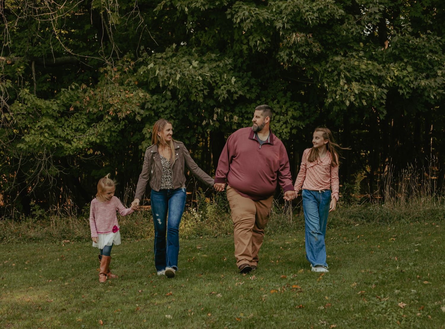 Family walking together through green summer meadow during outdoor photo session.