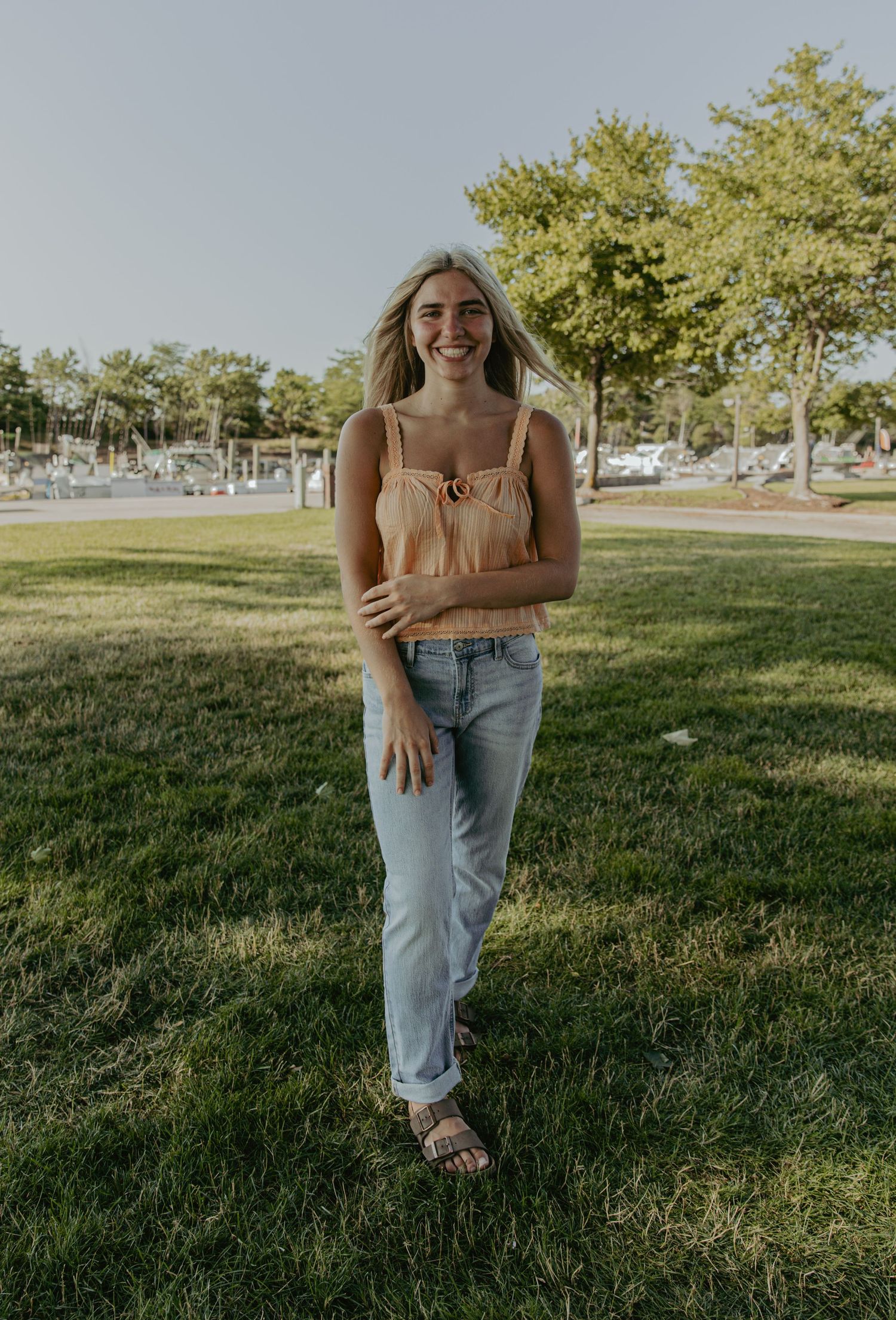 Woman in casual summer outfit standing on grass near marina.
