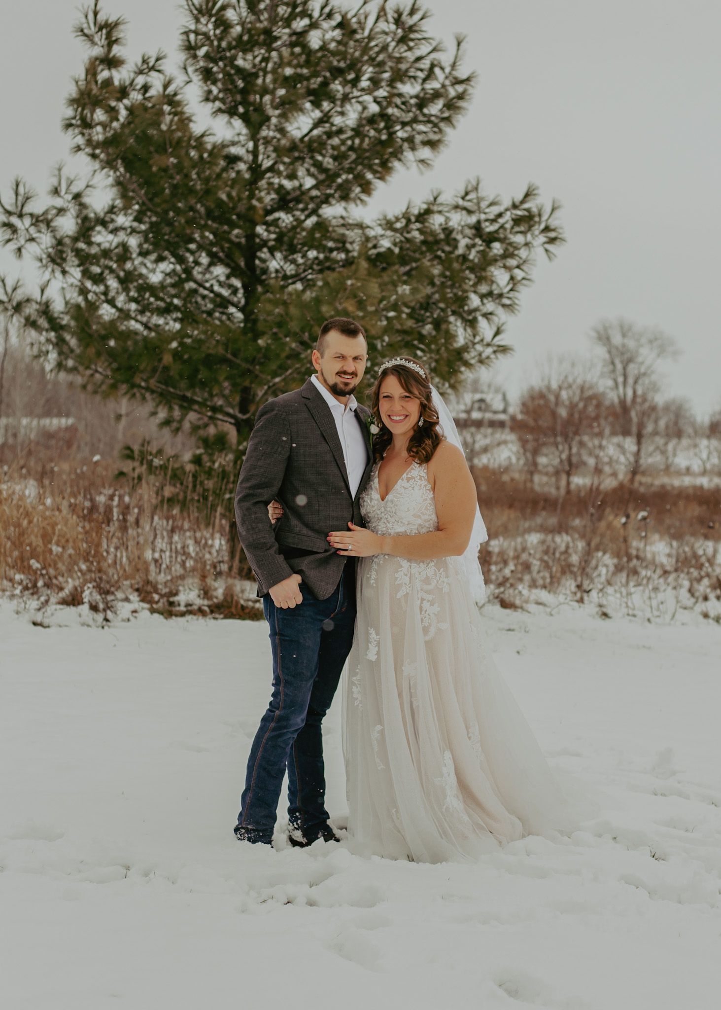 Winter wedding photography session in a snowy field with evergreen trees.