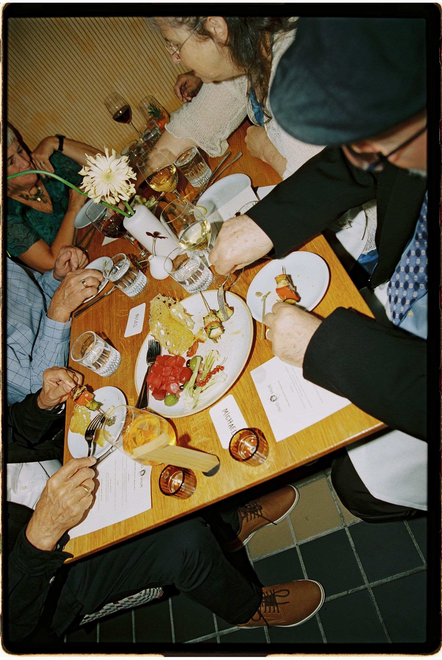 Overhead view of people dining at a restaurant table with plates of food, drinks, and menus on a wooden surface.
