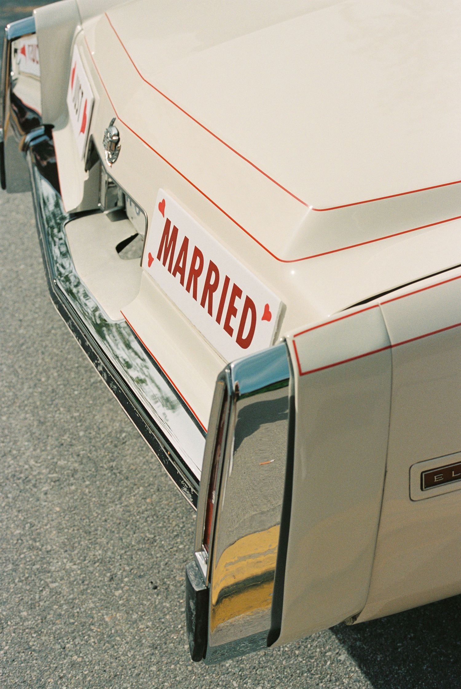 White vintage wedding car with red trim and a Just Married bumper sign, photographed from above on a sunny day.