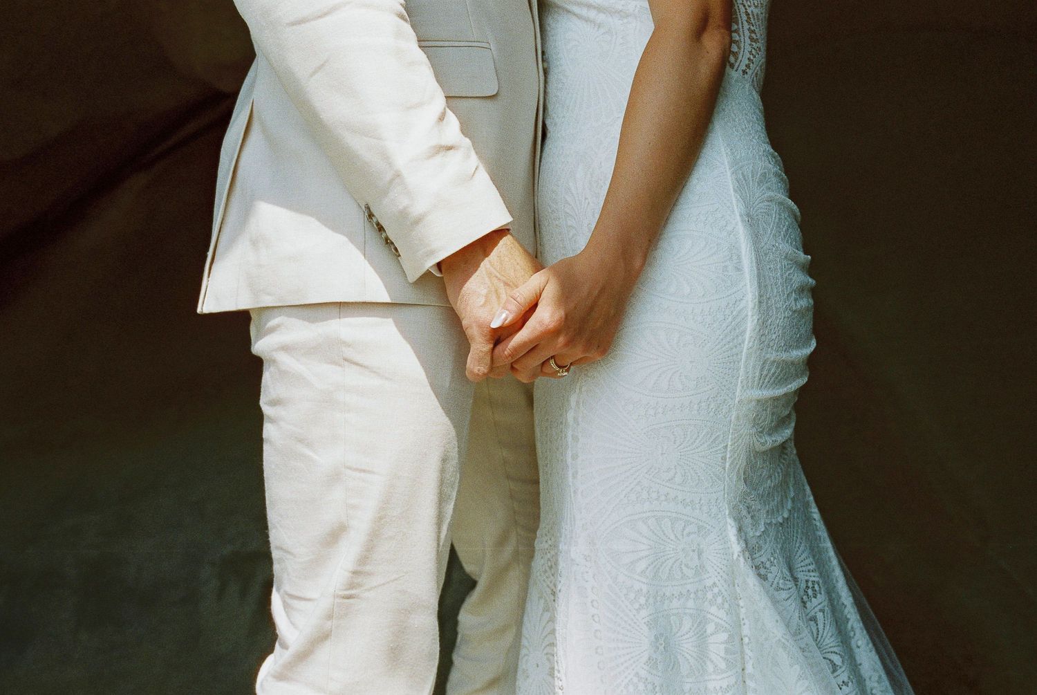 A close-up of a couple holding hands, both wearing white formal attire.