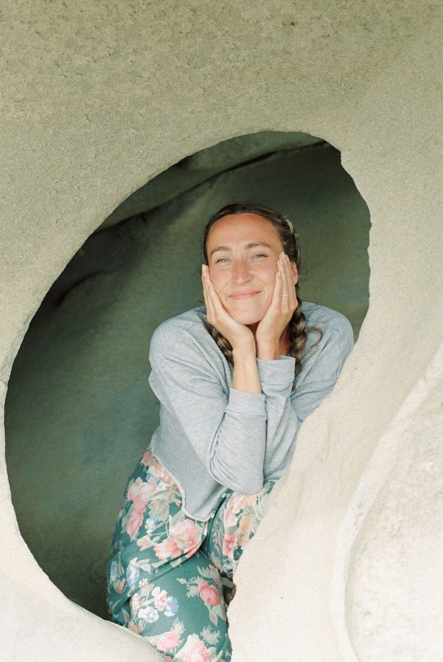 Joyful portrait through a curved opening showing someone in floral pants and grey sweater.