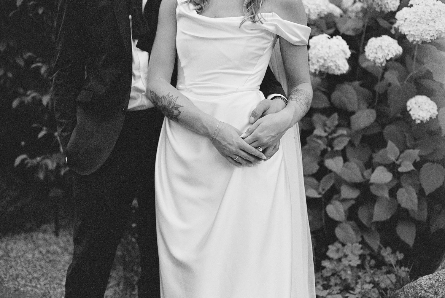 Black and white wedding photo showing couple's embrace with hydrangea bushes in background.