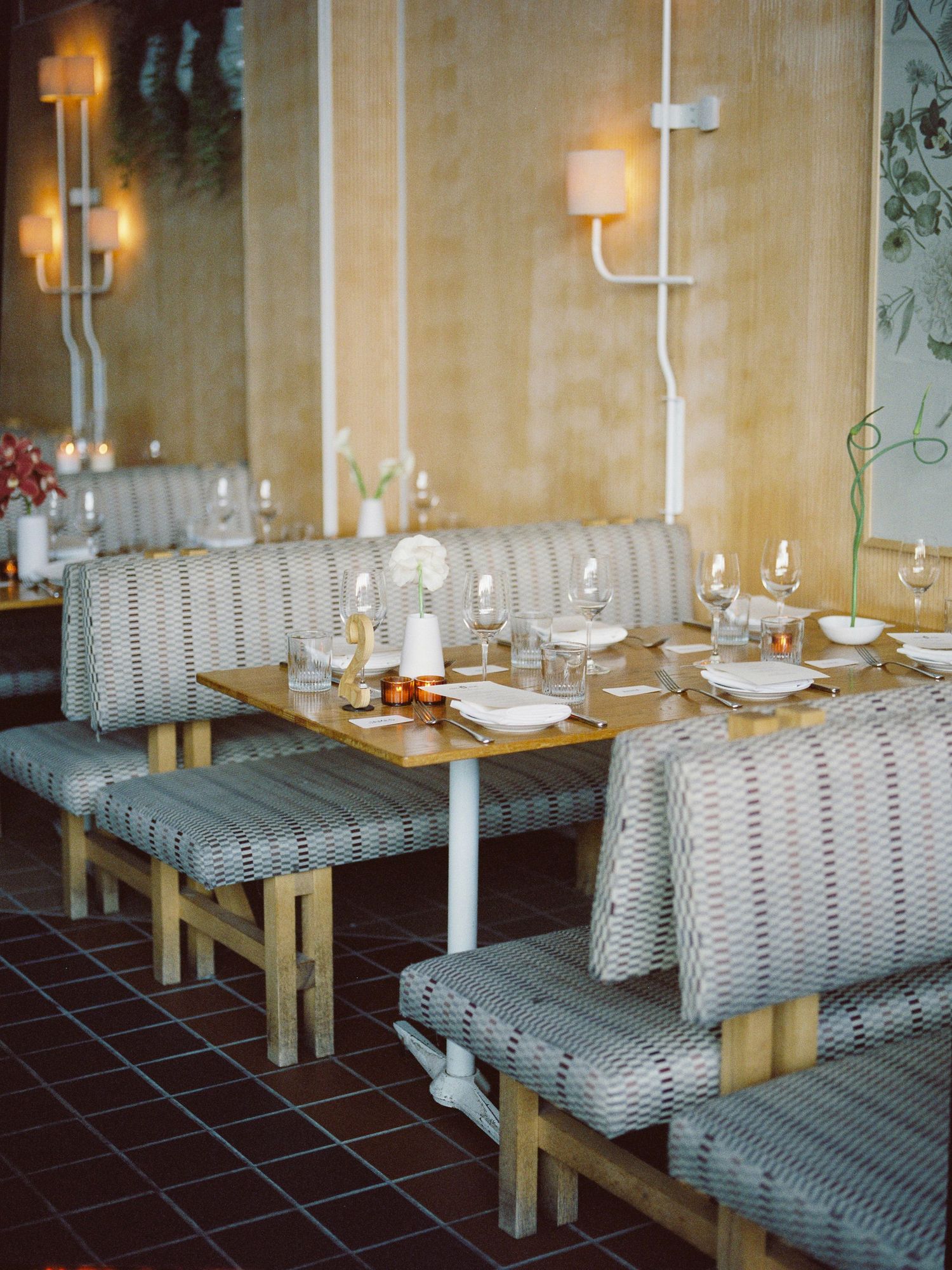Elegant restaurant booth seating with wicker benches, wooden tables set with glassware, and warm wall sconces.