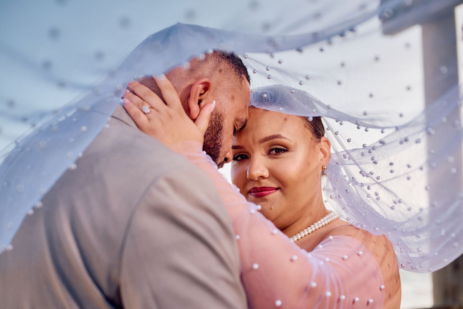 Bride and groom share an intimate moment under a pearl-studded veil on their wedding day.