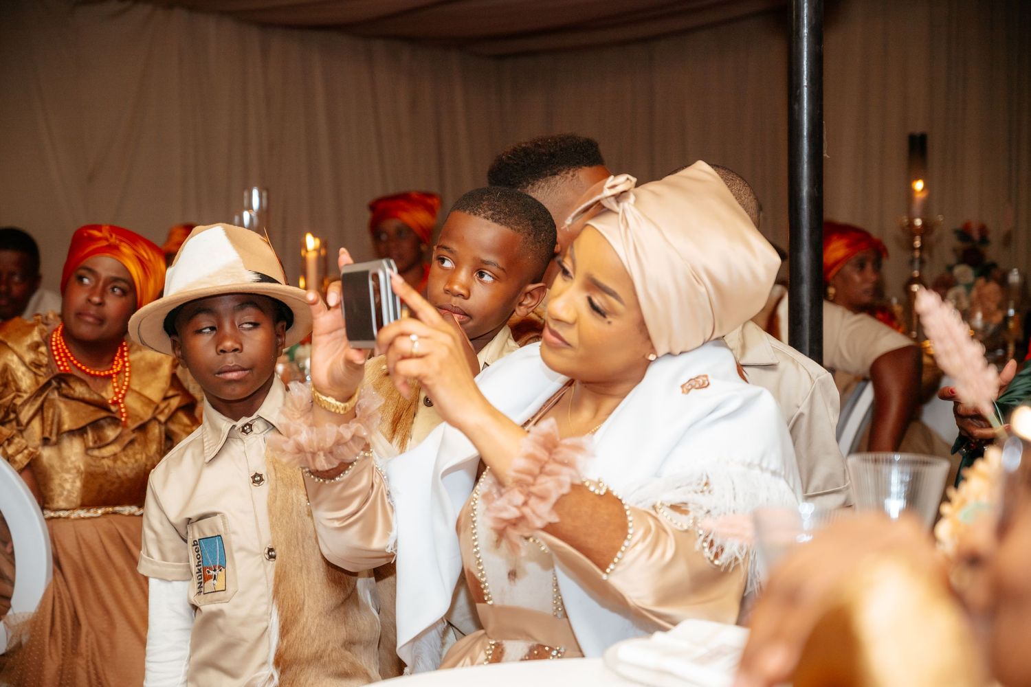 Woman in hijab and children in safari outfits taking photos at a festive indoor celebration event.