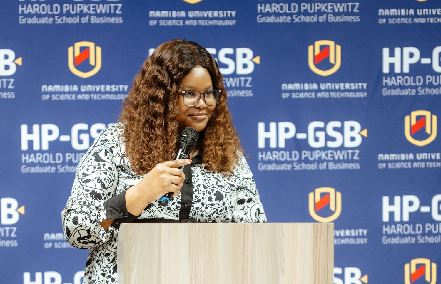 Woman speaking at podium at HP-GSB Harold Pupkewitz Graduate School of Business event in Namibia.