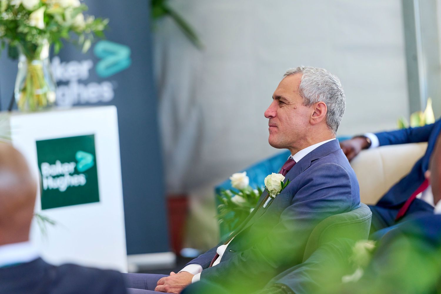 Executive listening attentively at a Baker Hughes corporate event with branded signage in background.