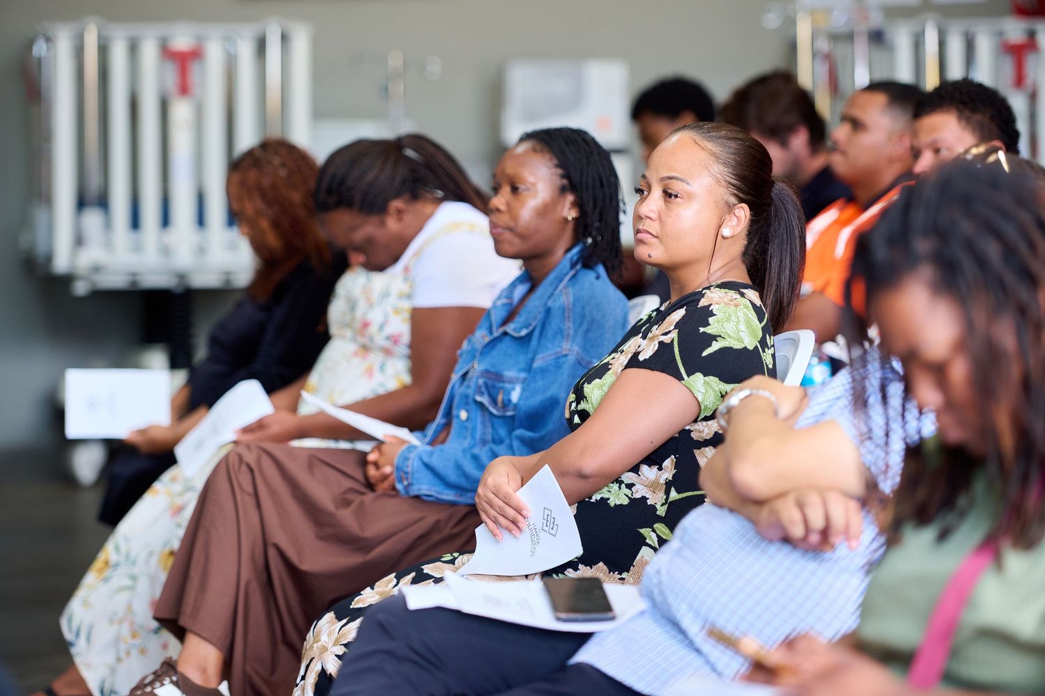 Diverse group of people sitting in rows at an indoor event, attentively listening and taking notes.