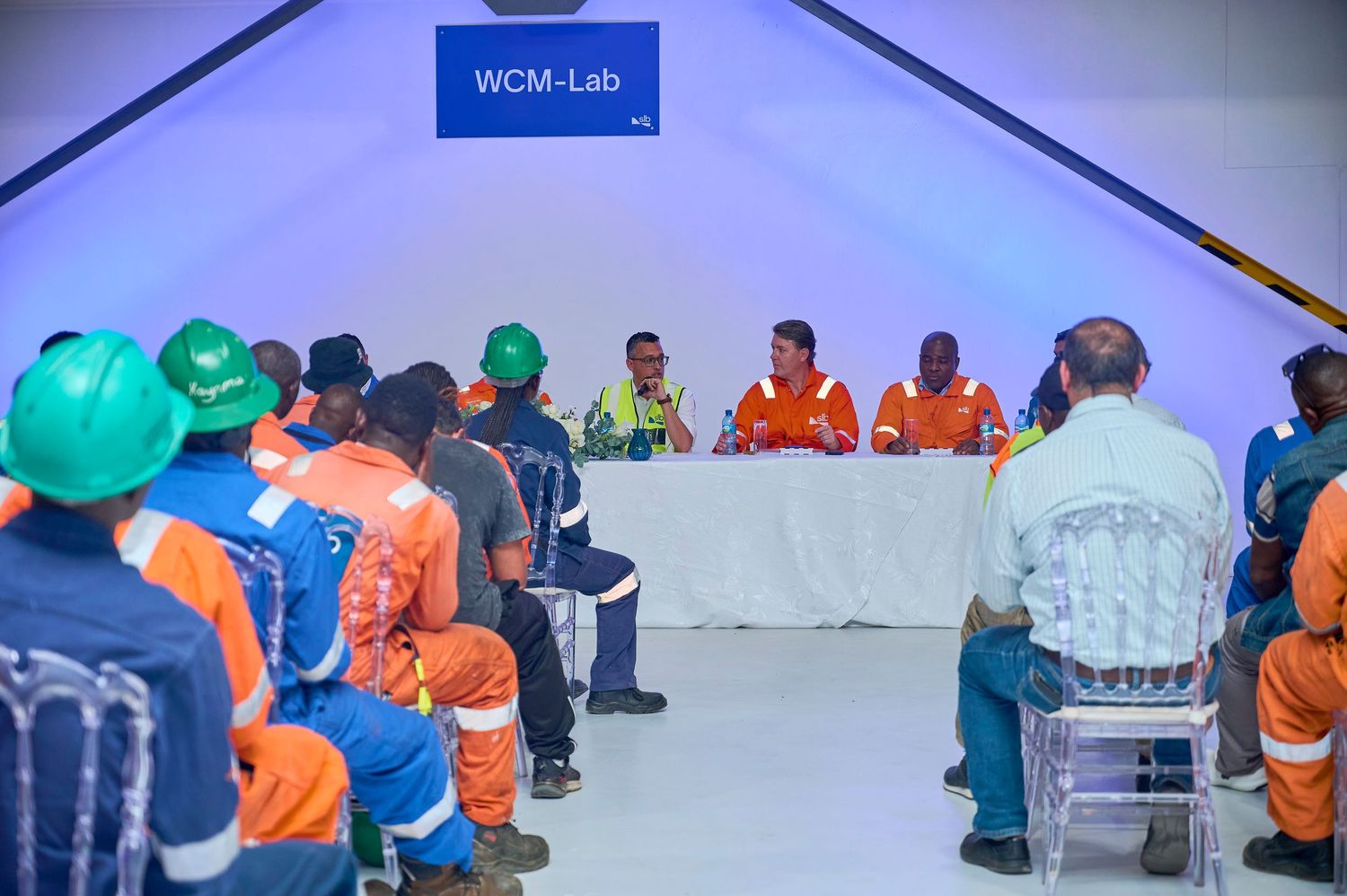 Workers in safety gear attend a WCM-Lab meeting inside a tent facility.