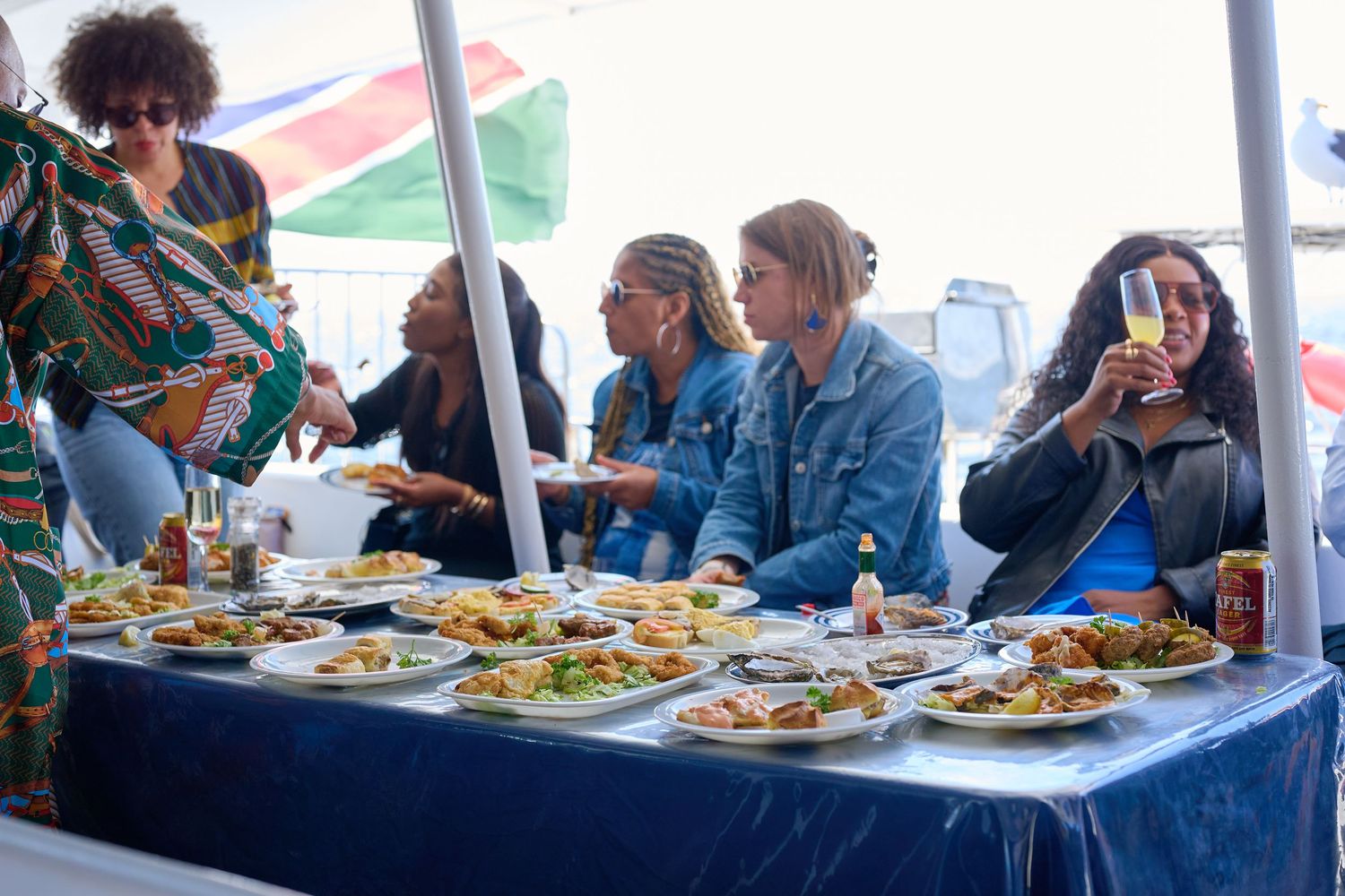 Women gathered around a table filled with plates of food at an outdoor event under a white tent.