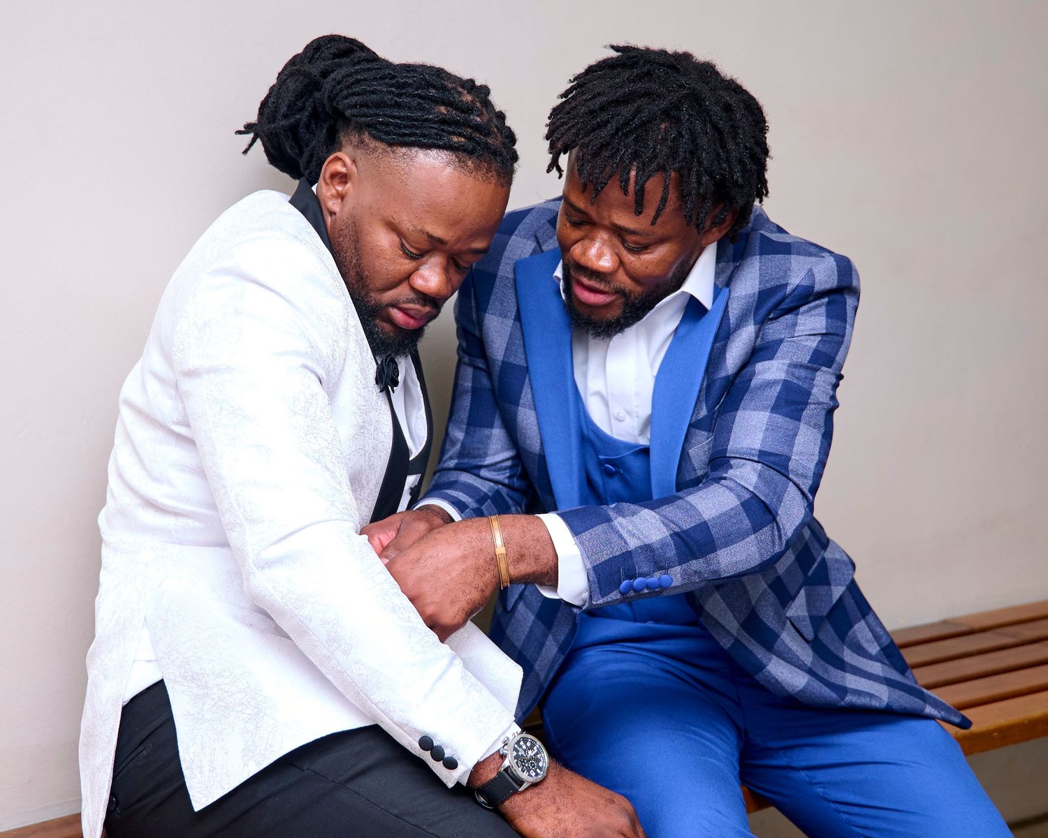 Two men in stylish suits, one white and one blue plaid, sitting together in a candid moment.