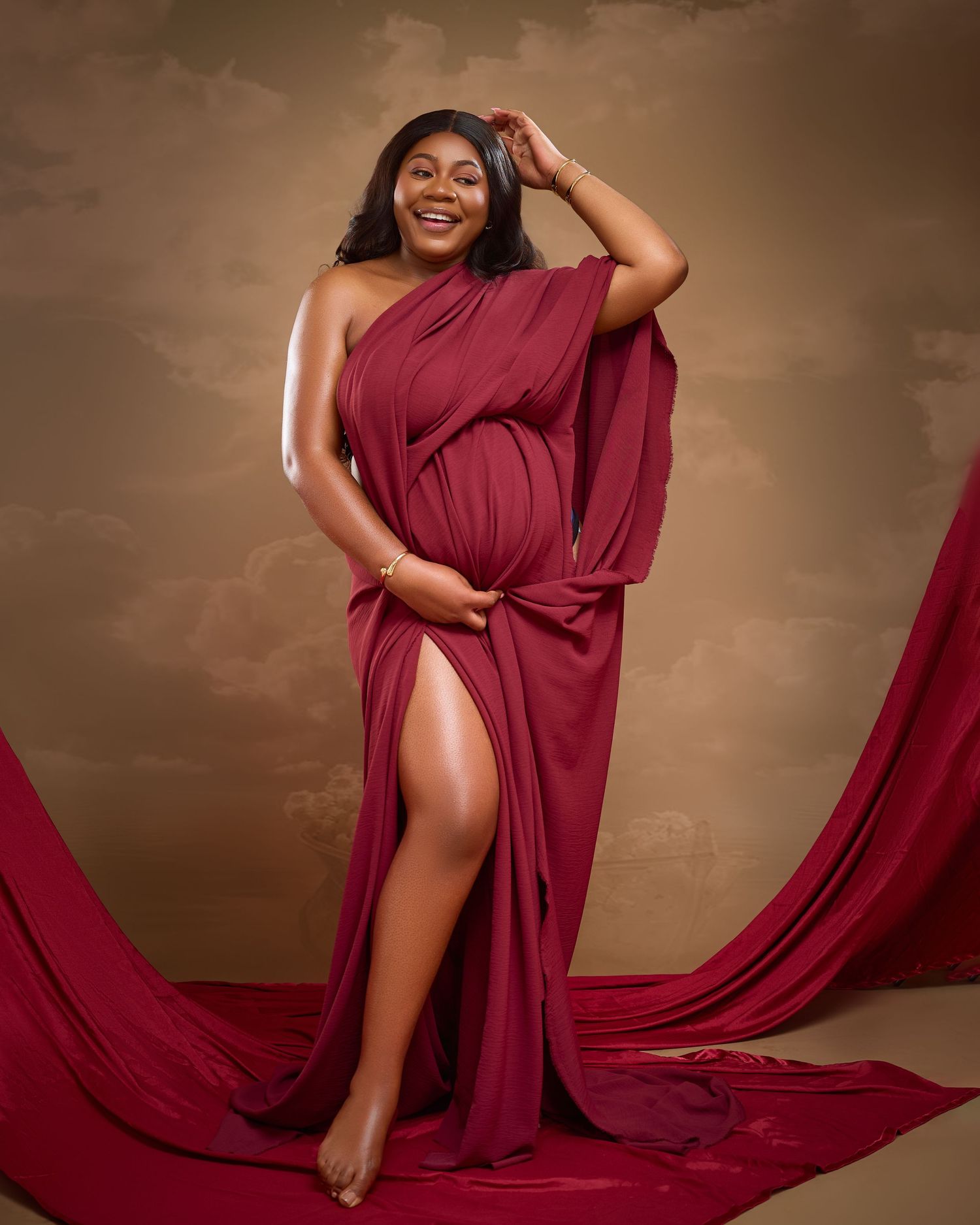 A flowing burgundy red dress fabric drapes elegantly across a dark brown studio backdrop creating dramatic movement.
