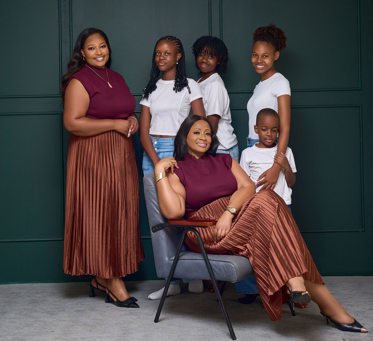 A family of six poses for a portrait, with two women in burgundy outfits and four children in white shirts.