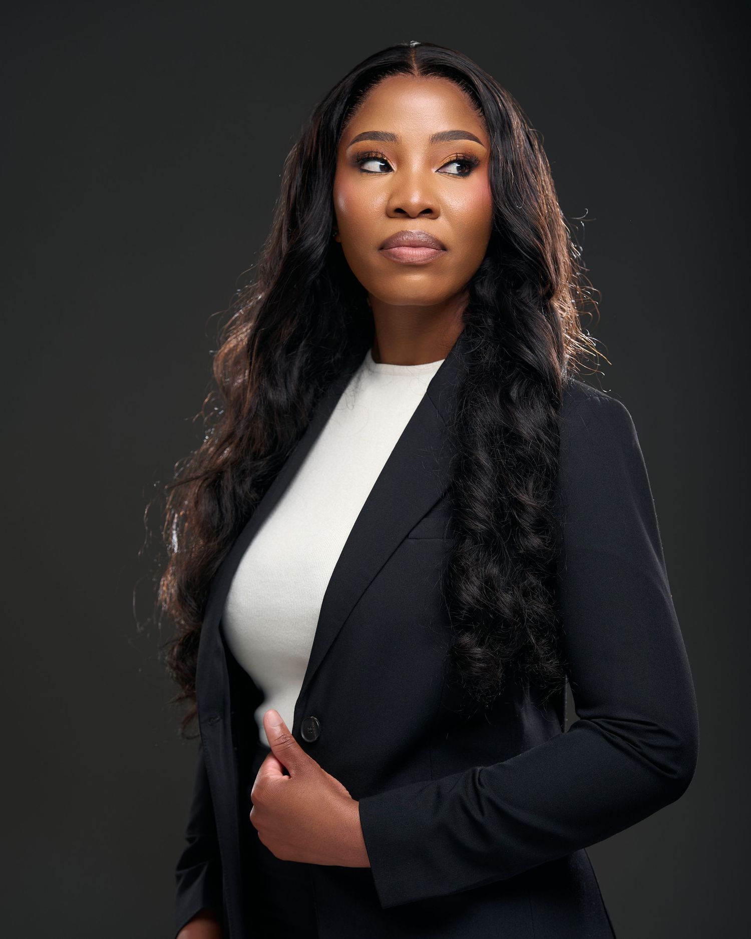 A professional woman in a black blazer and white top poses confidently against a dark studio background.