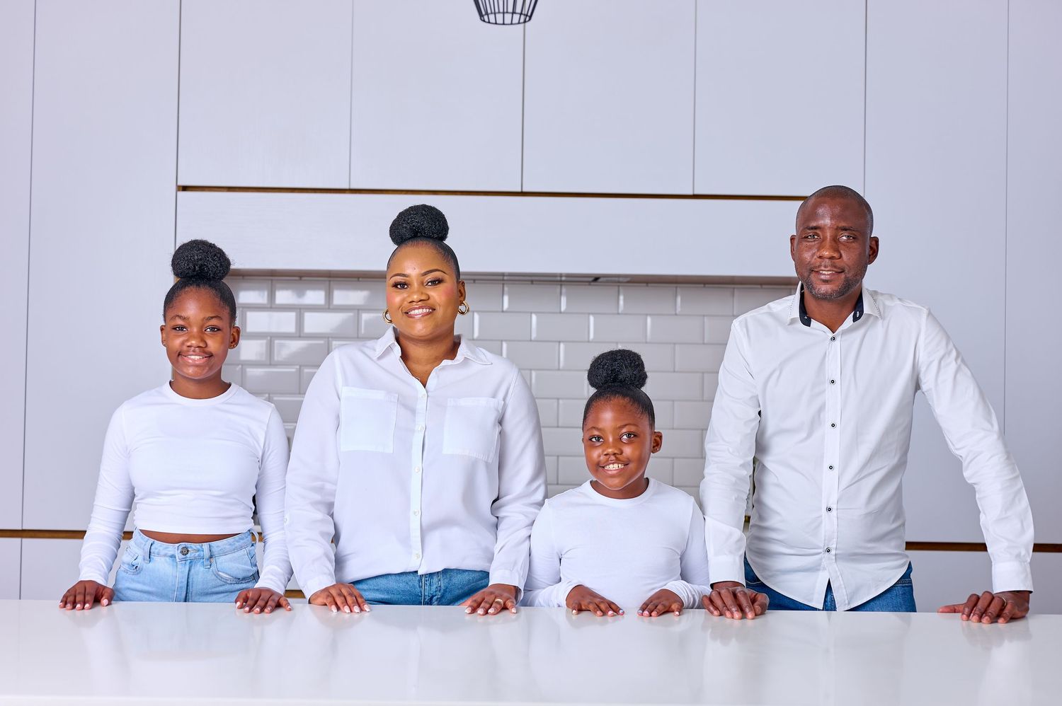 Happy family of four standing together in modern white kitchen smiling at camera.
