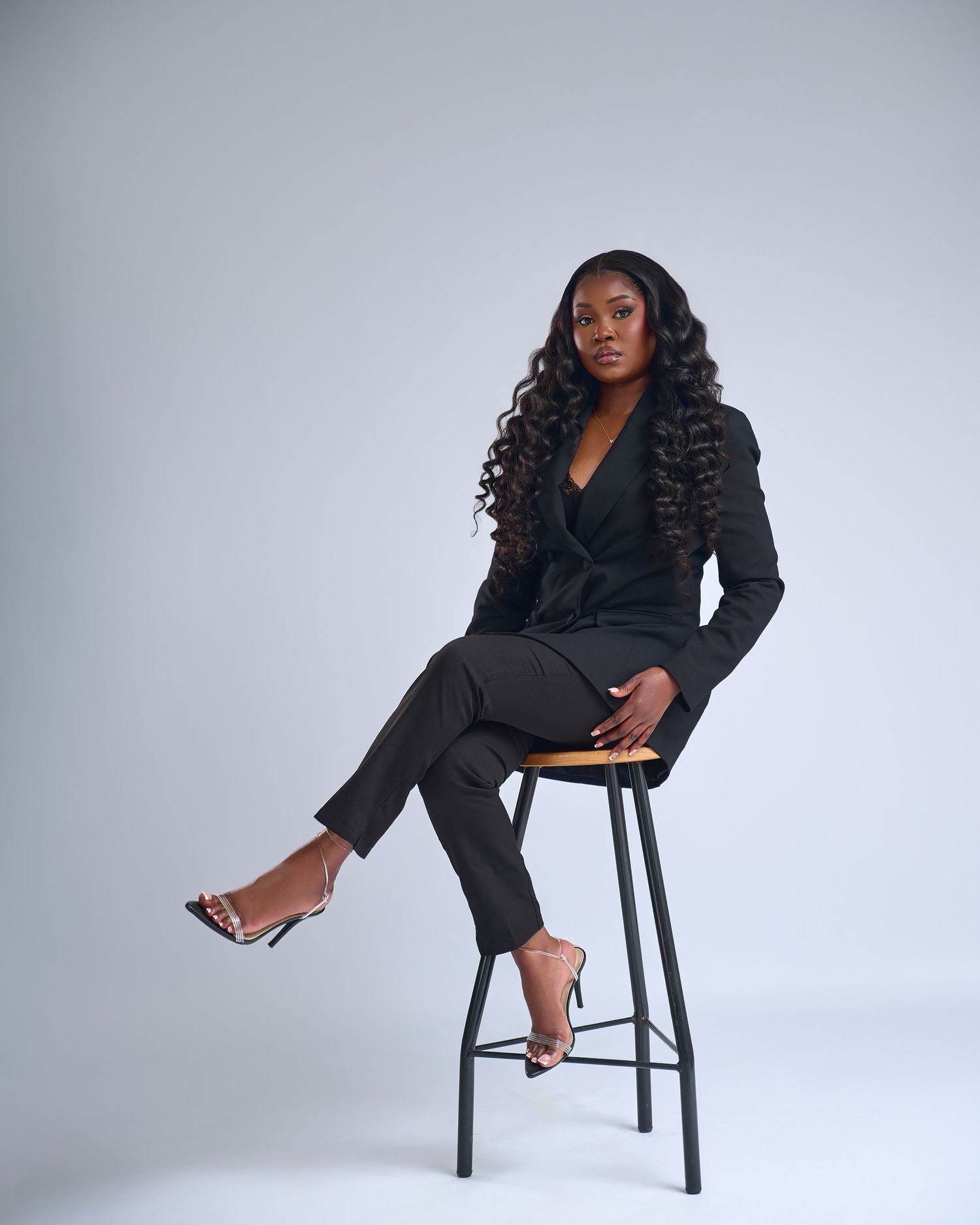 Model in black blazer and shorts strikes dynamic poses on wooden chair against white studio backdrop.