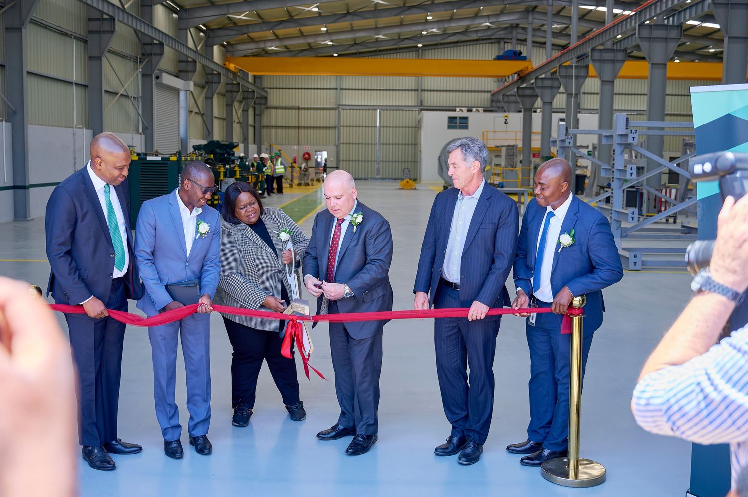 Officials cutting a red ribbon at a Baker Hughes facility grand opening ceremony in an industrial warehouse.