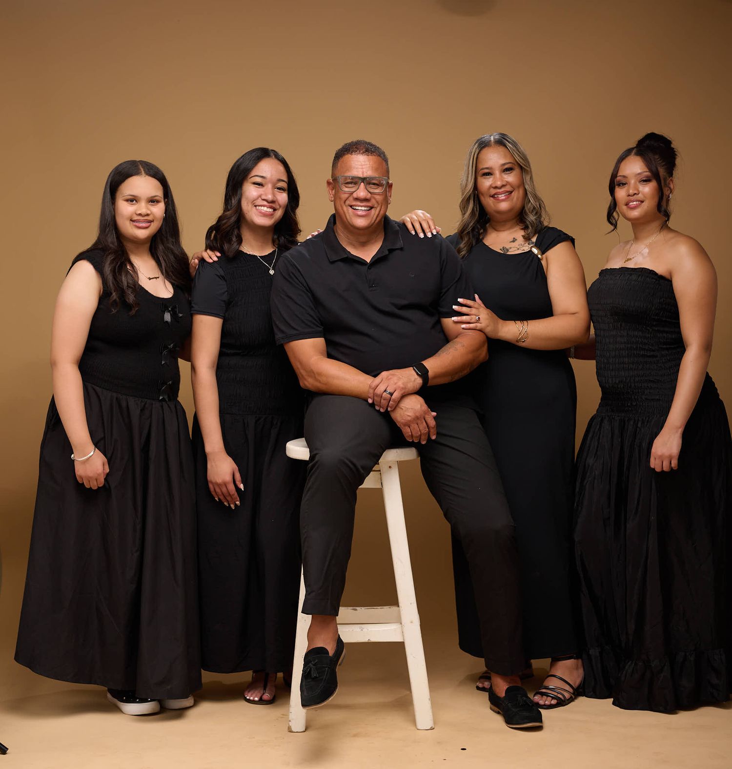 Group wearing black formal attire poses together on brown background in studio setting.
