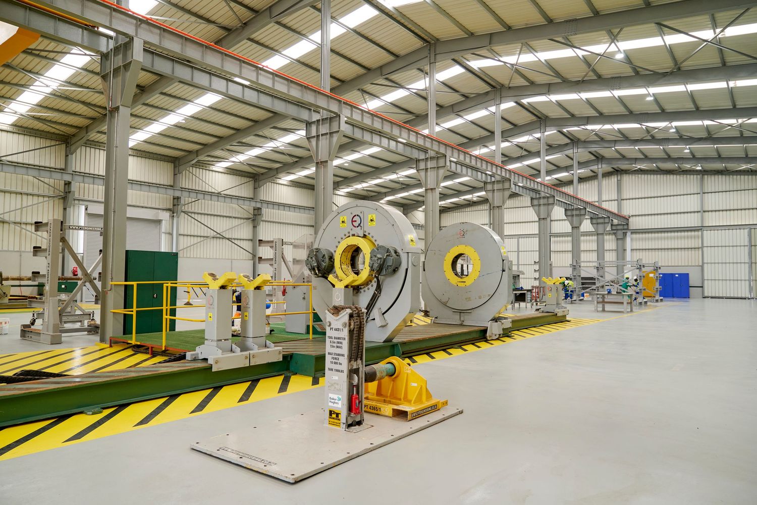 Large industrial warehouse with steel coil reels and yellow machinery on a spacious factory floor.