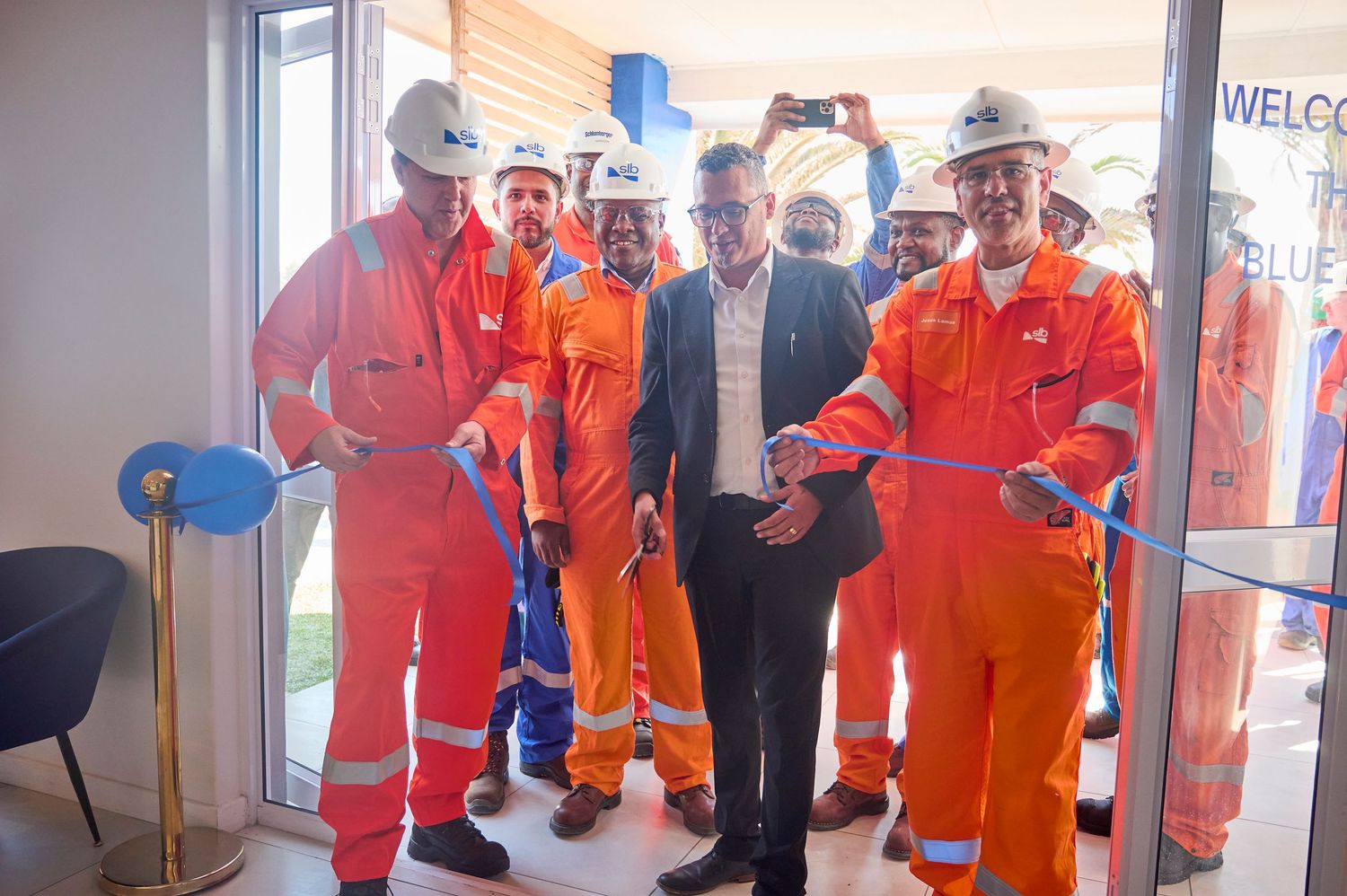 Workers in orange safety gear cut a blue ribbon at a facility opening ceremony with a suited official.