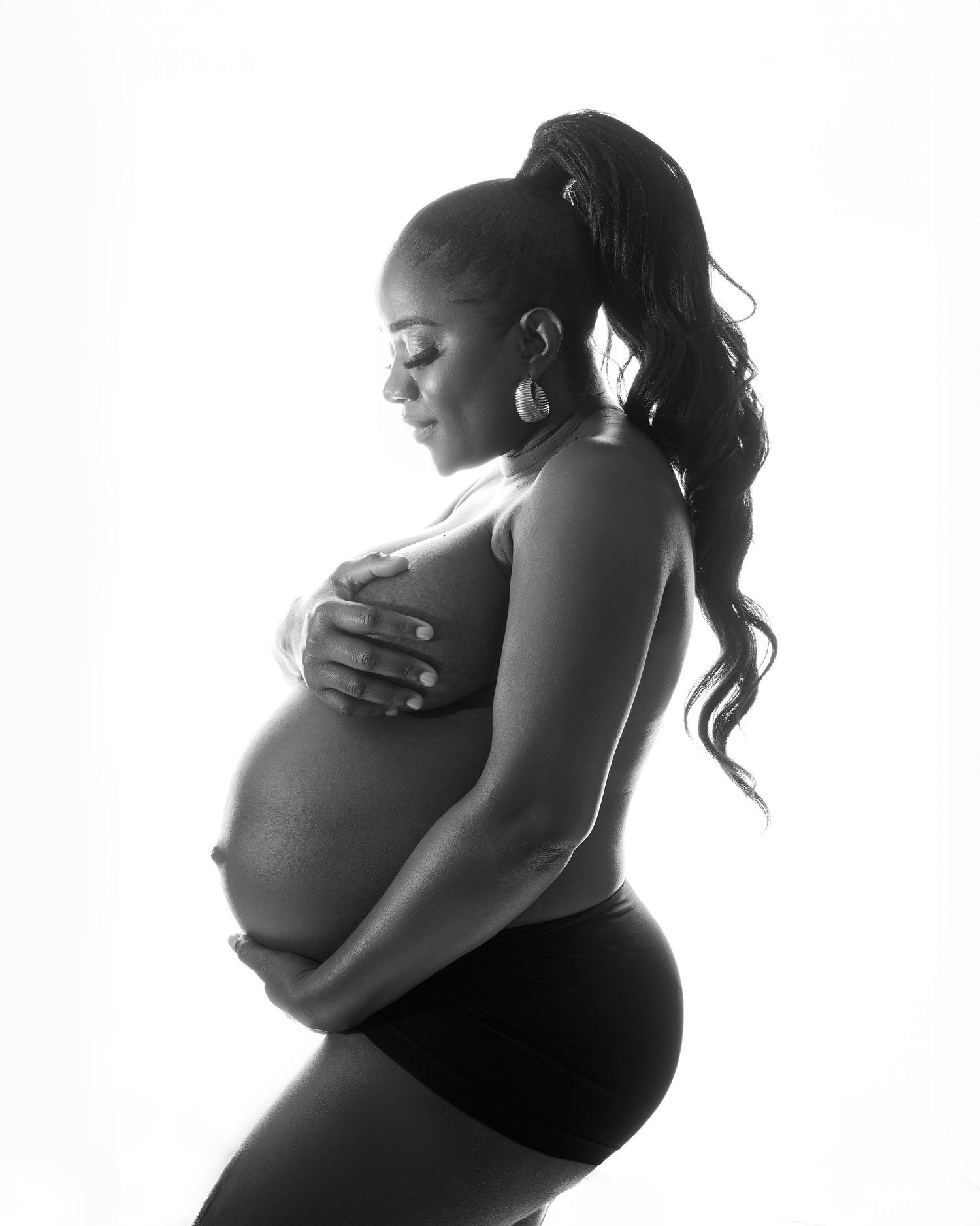 Black and white silhouette portraits of a pregnant woman in different poses showing her baby bump.