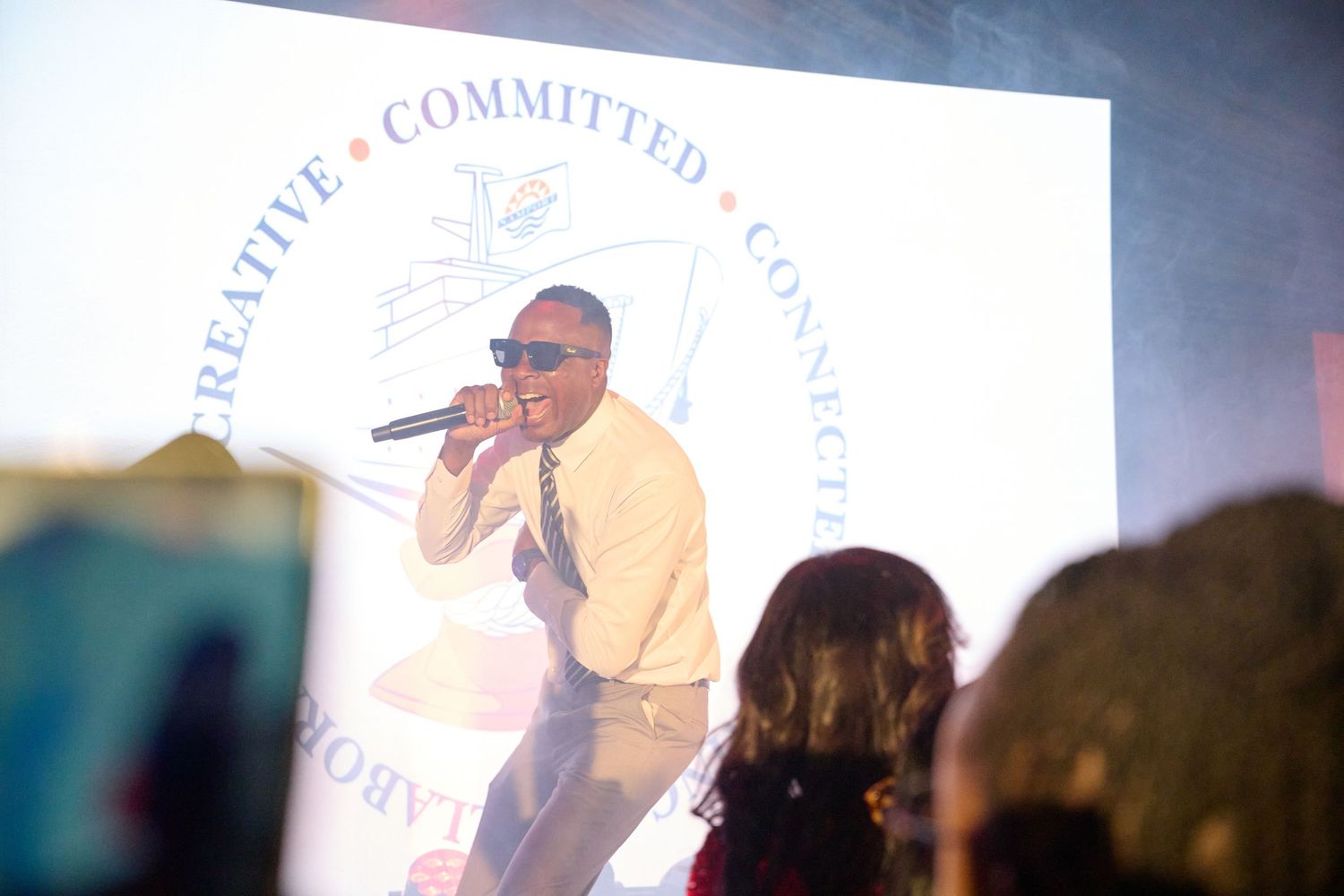 Man performing on stage with microphone at a creative committed connected event with banner backdrop.