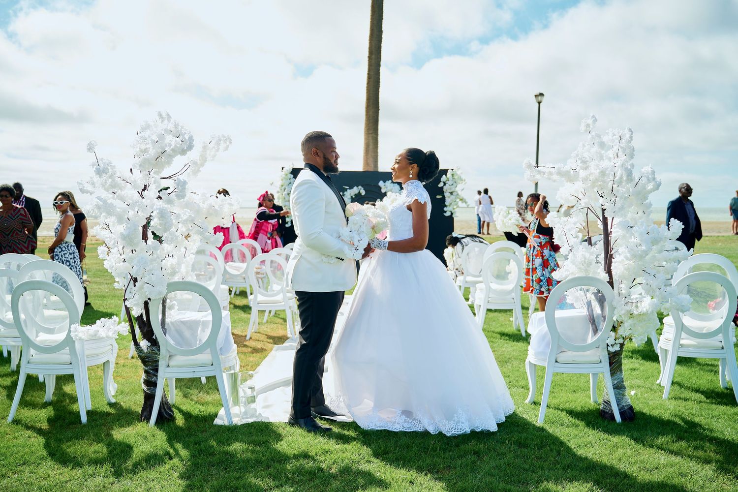 Bride and groom share a romantic moment at an outdoor wedding ceremony with white chairs and floral decorations.