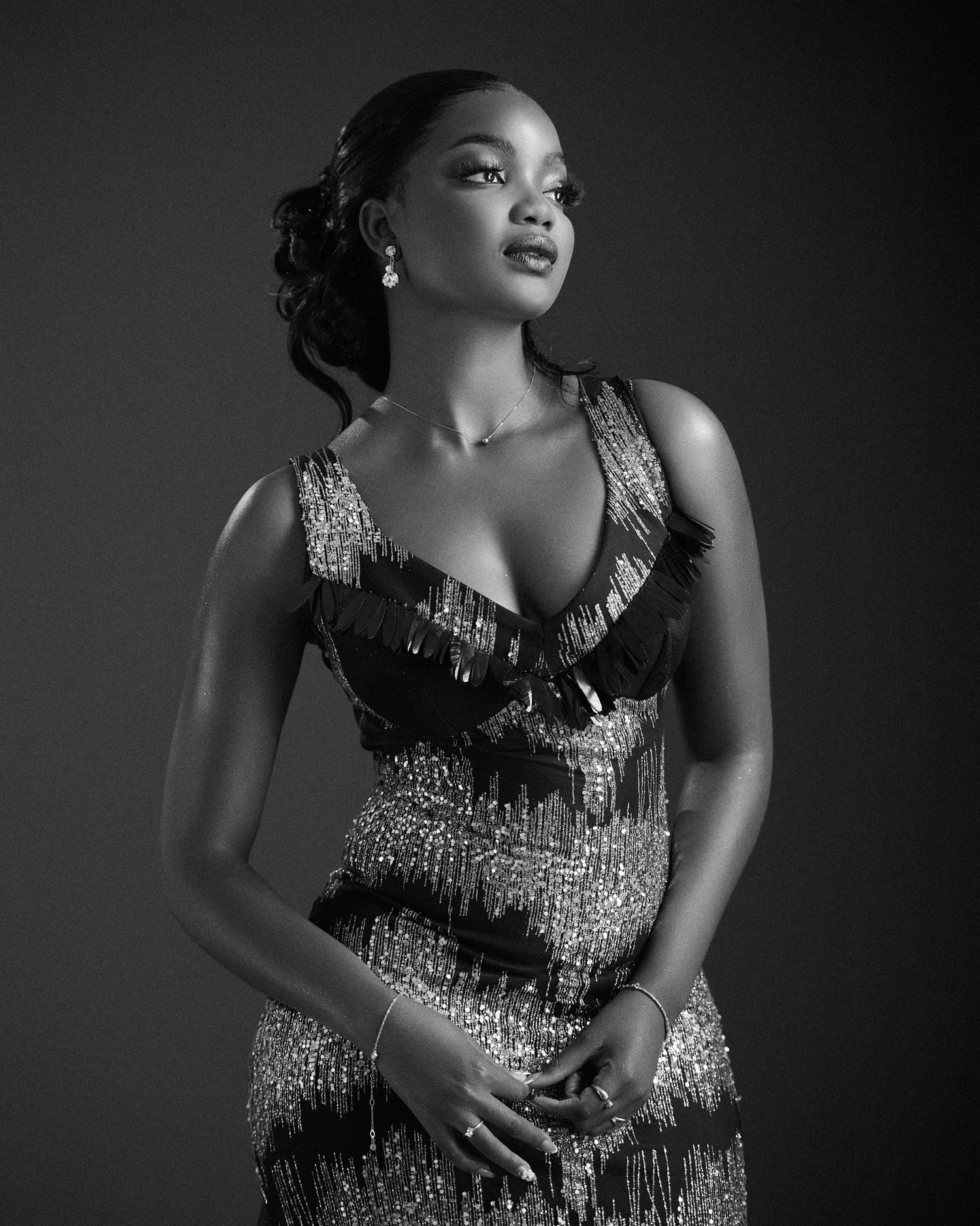 Black and white portrait photograph showing an elegant figure in a sequined dress with a sweetheart neckline against dark backdrop.