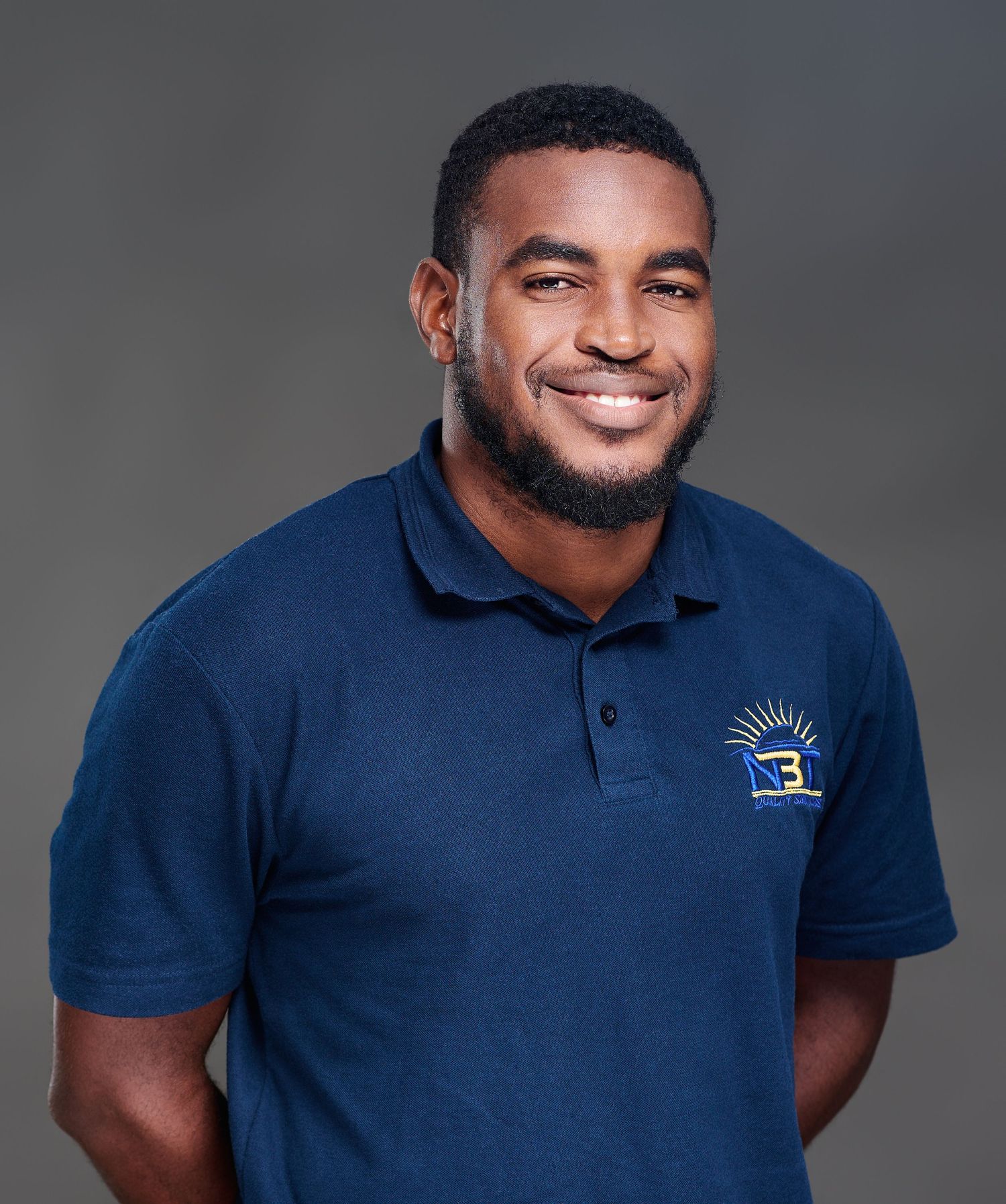 Smiling man in navy blue polo shirt with logo, professional headshot on gray background.