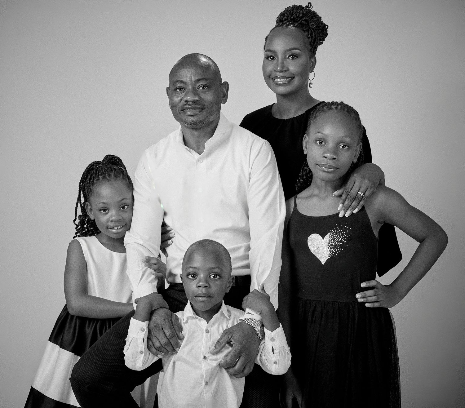 Black and white family portrait of parents with three young children posing together in a professional studio setting.