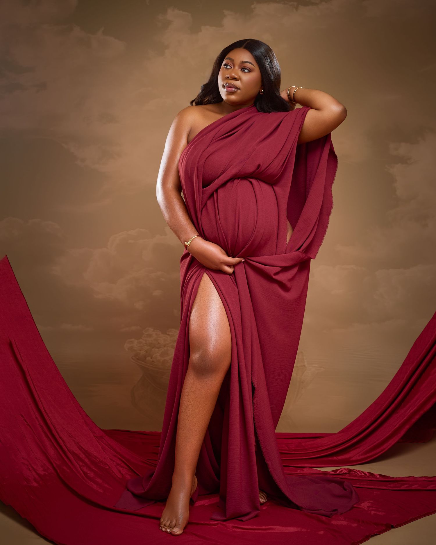 A flowing burgundy dress elegantly drapes across a maternity photoshoot set with dramatic lighting.
