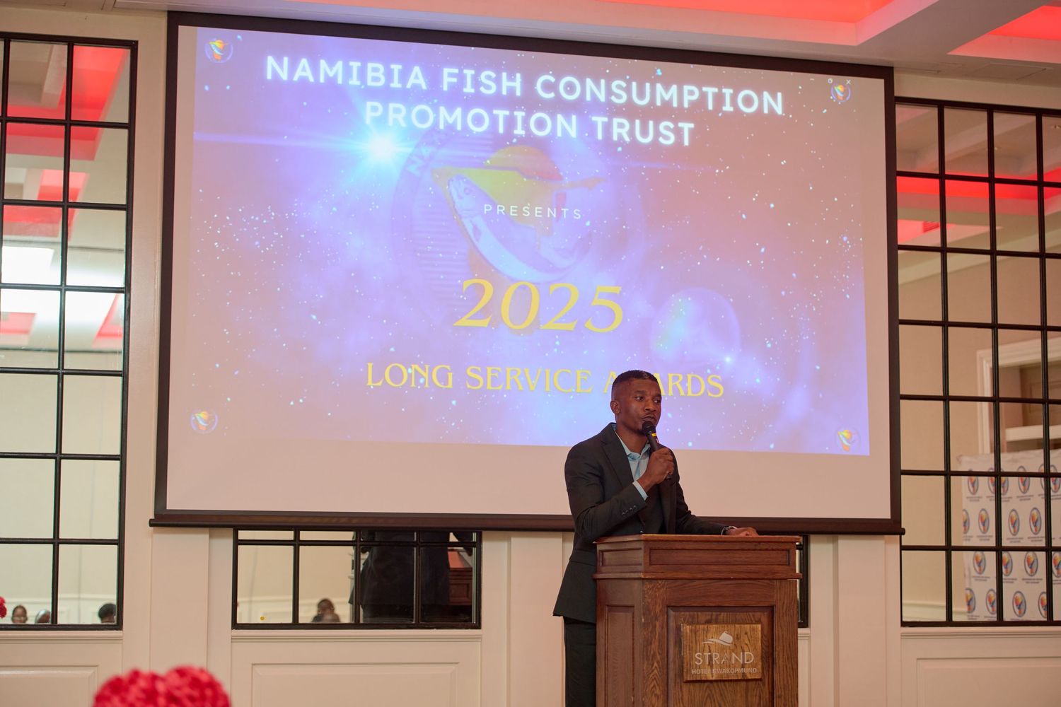 A man speaks at a podium during the 2025 Namibia Fish Consumption Promotion Trust Long Service Awards ceremony.