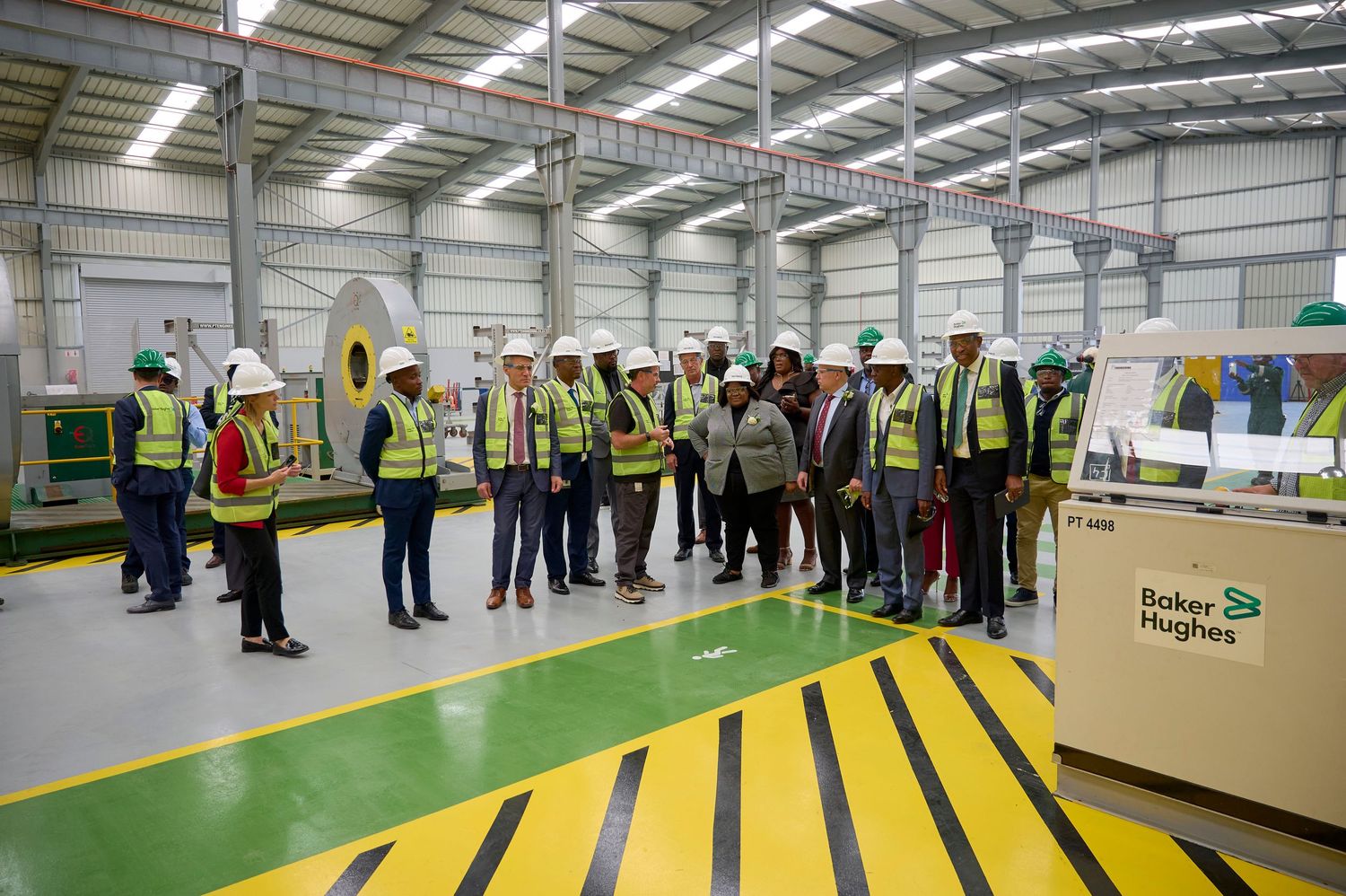Group of professionals in hard hats touring a Baker Hughes manufacturing facility with industrial equipment.