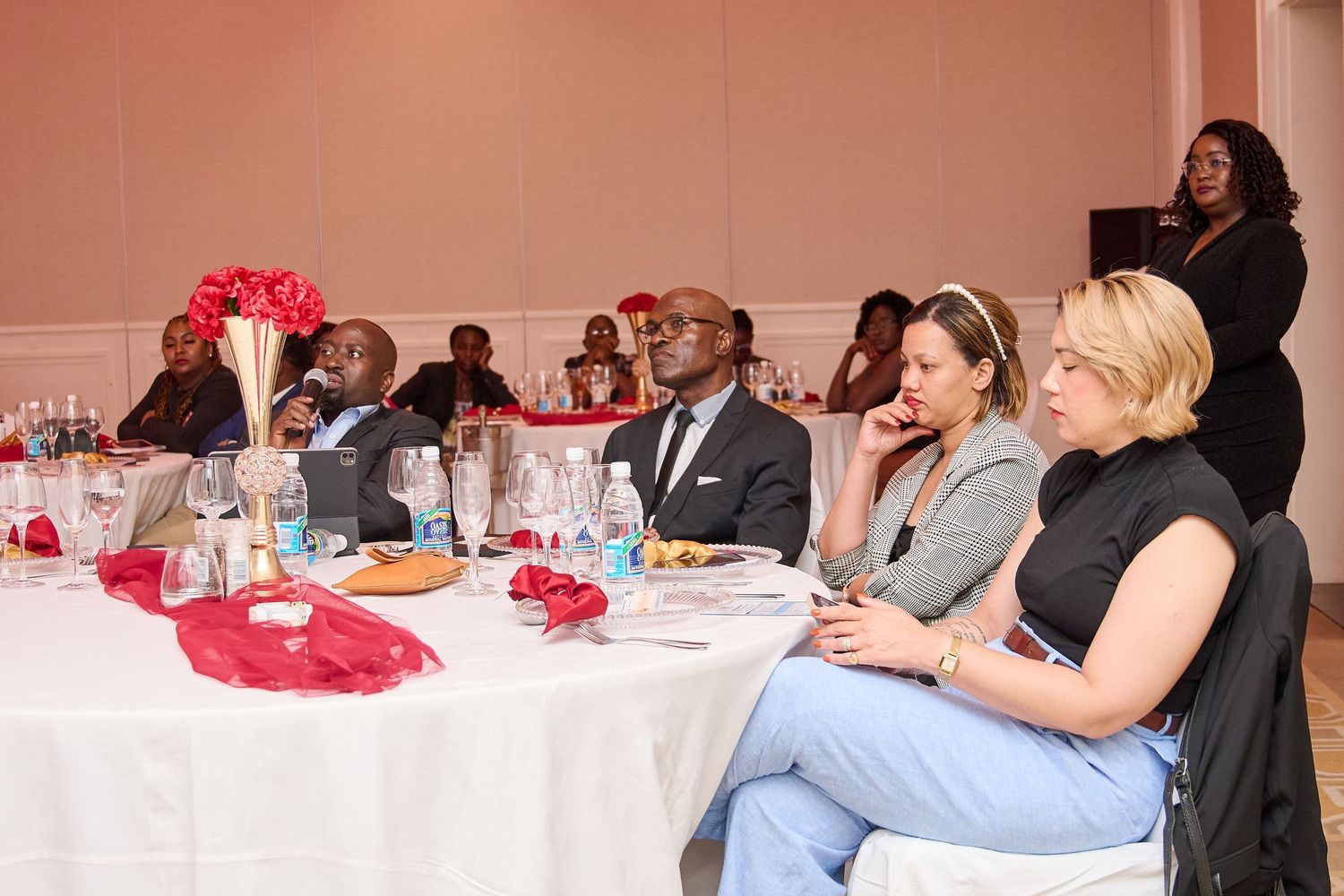 Diverse group of professionals seated at banquet tables during a formal conference or corporate event in a decorated hall.