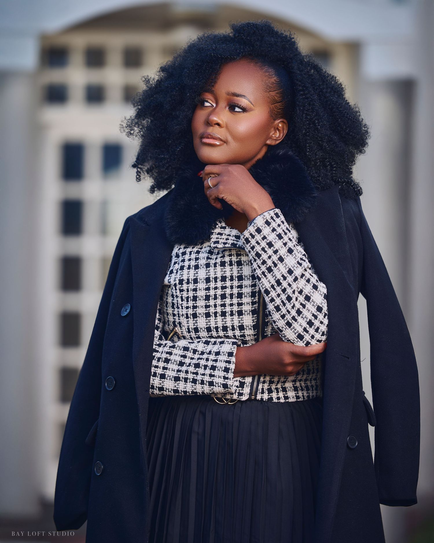 A stylish fashion portrait showing a black coat paired with a houndstooth scarf against an architectural backdrop.
