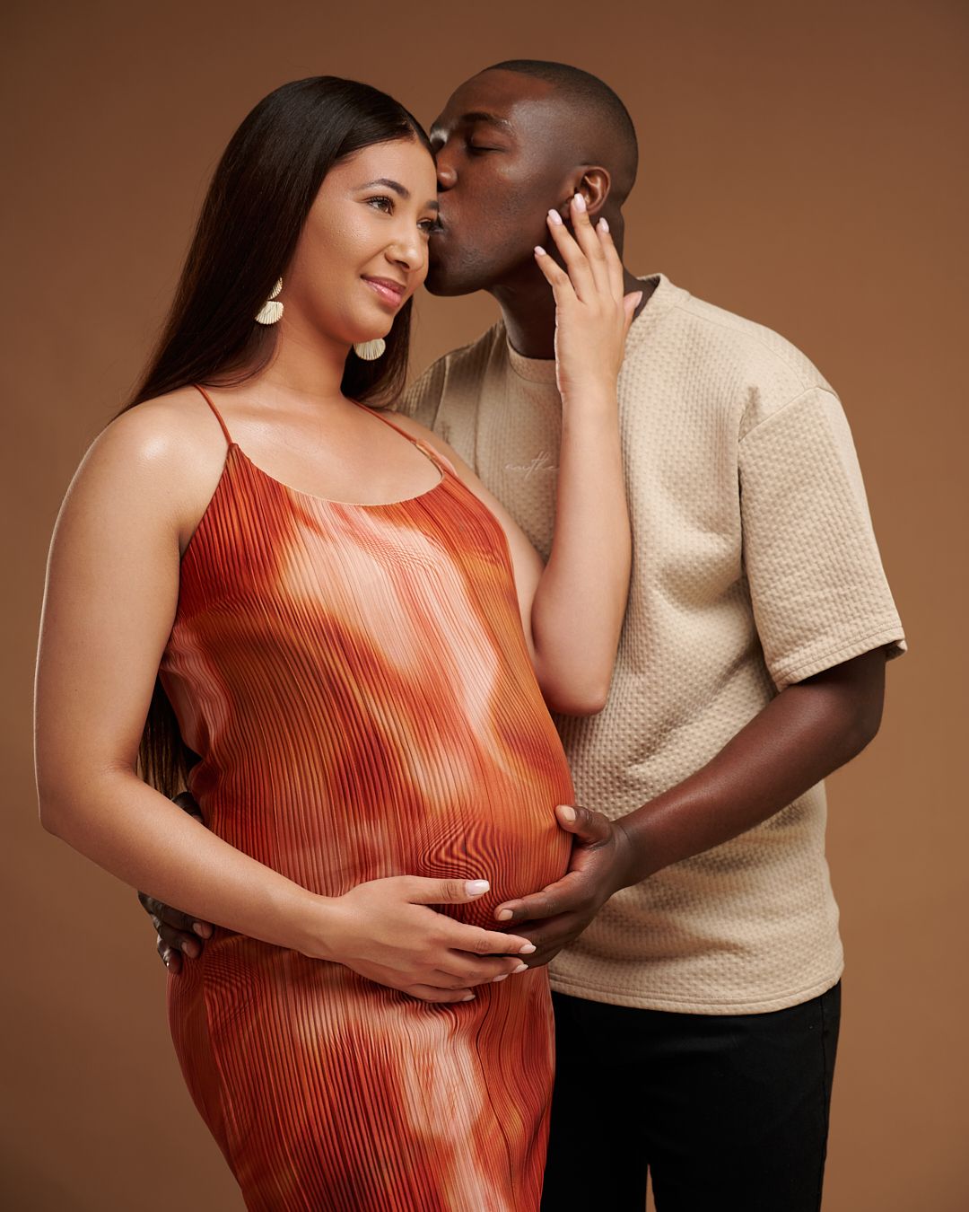 A romantic couple in coordinating orange and beige outfits embrace in a series of intimate studio portraits.