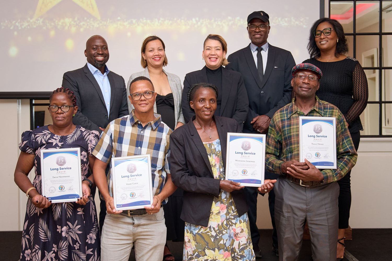 Group of award recipients posing with certificates at a formal recognition ceremony indoors.