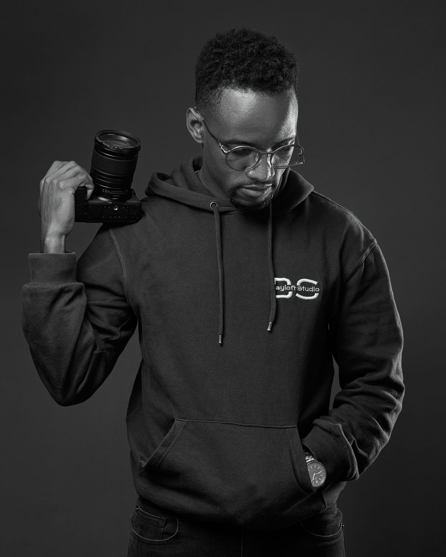 Black and white series of a person in a dark hoodie posing against a dark background.