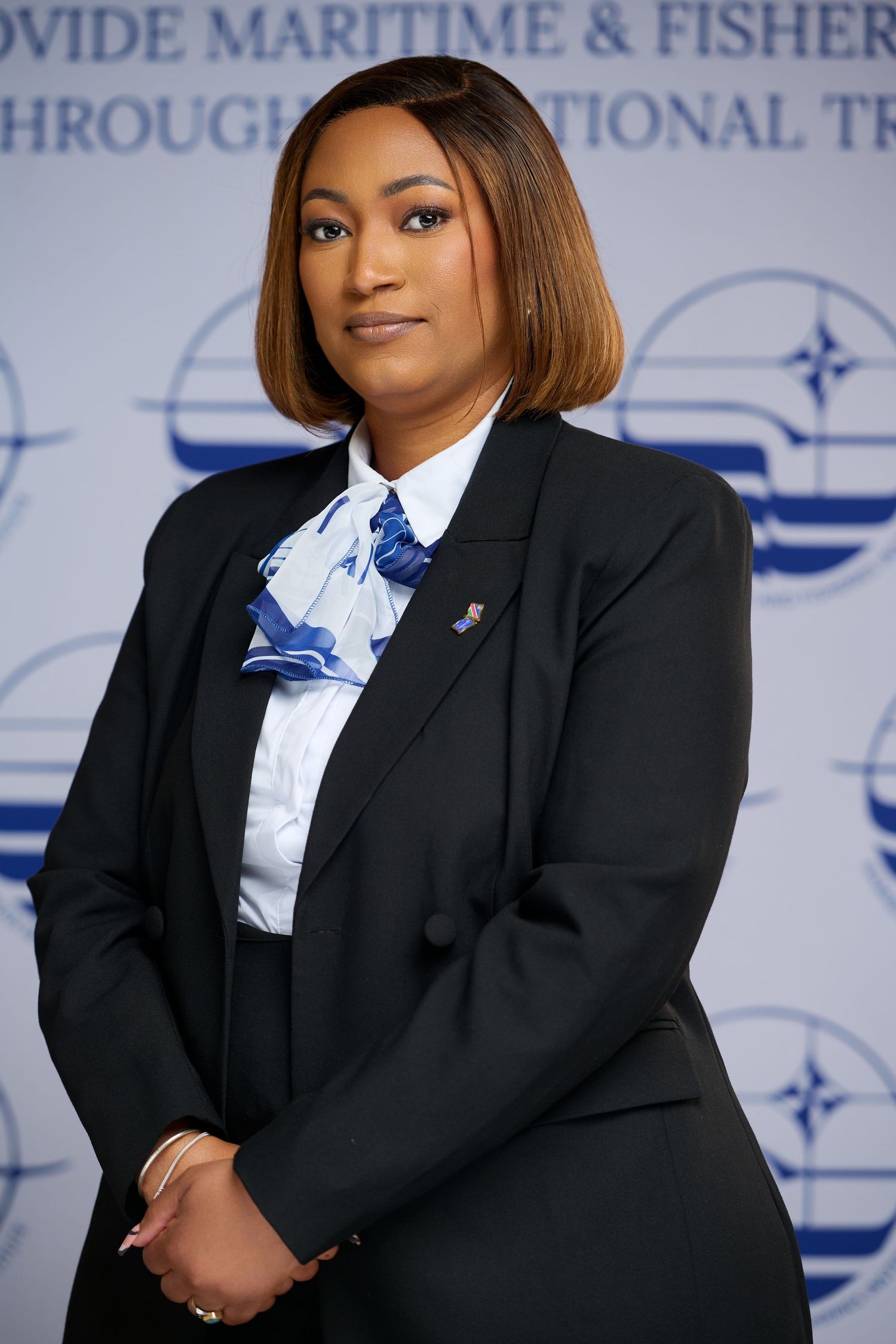 Professional woman in black blazer and blue bow tie stands before a maritime organization backdrop.