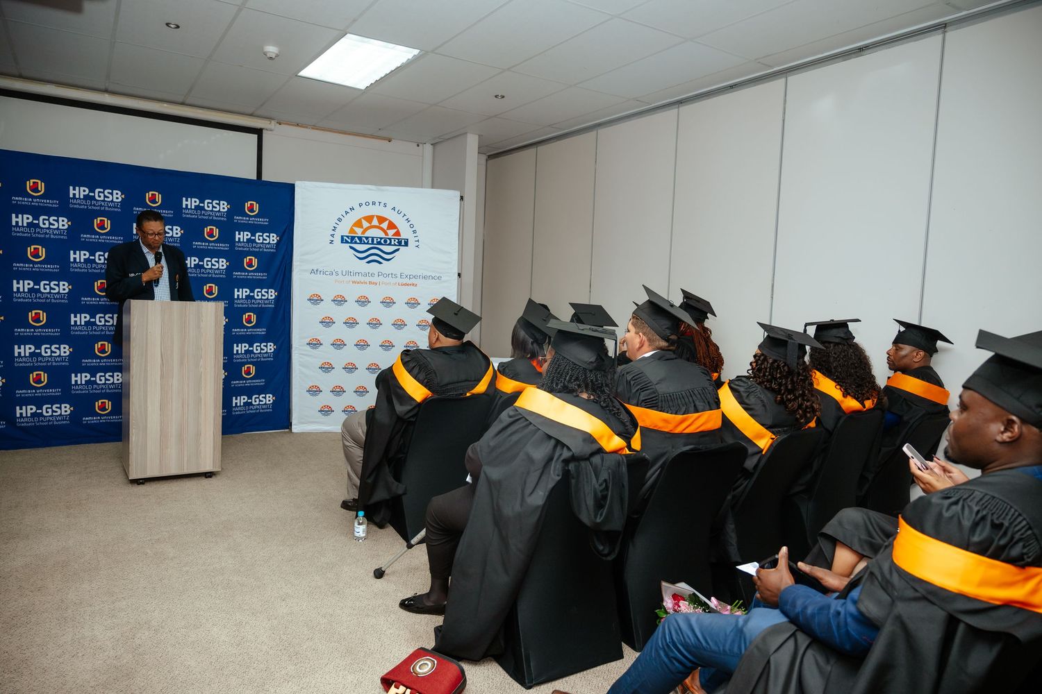 Speaker addresses graduates in caps and gowns at HP-GSB Namibia University graduation event.