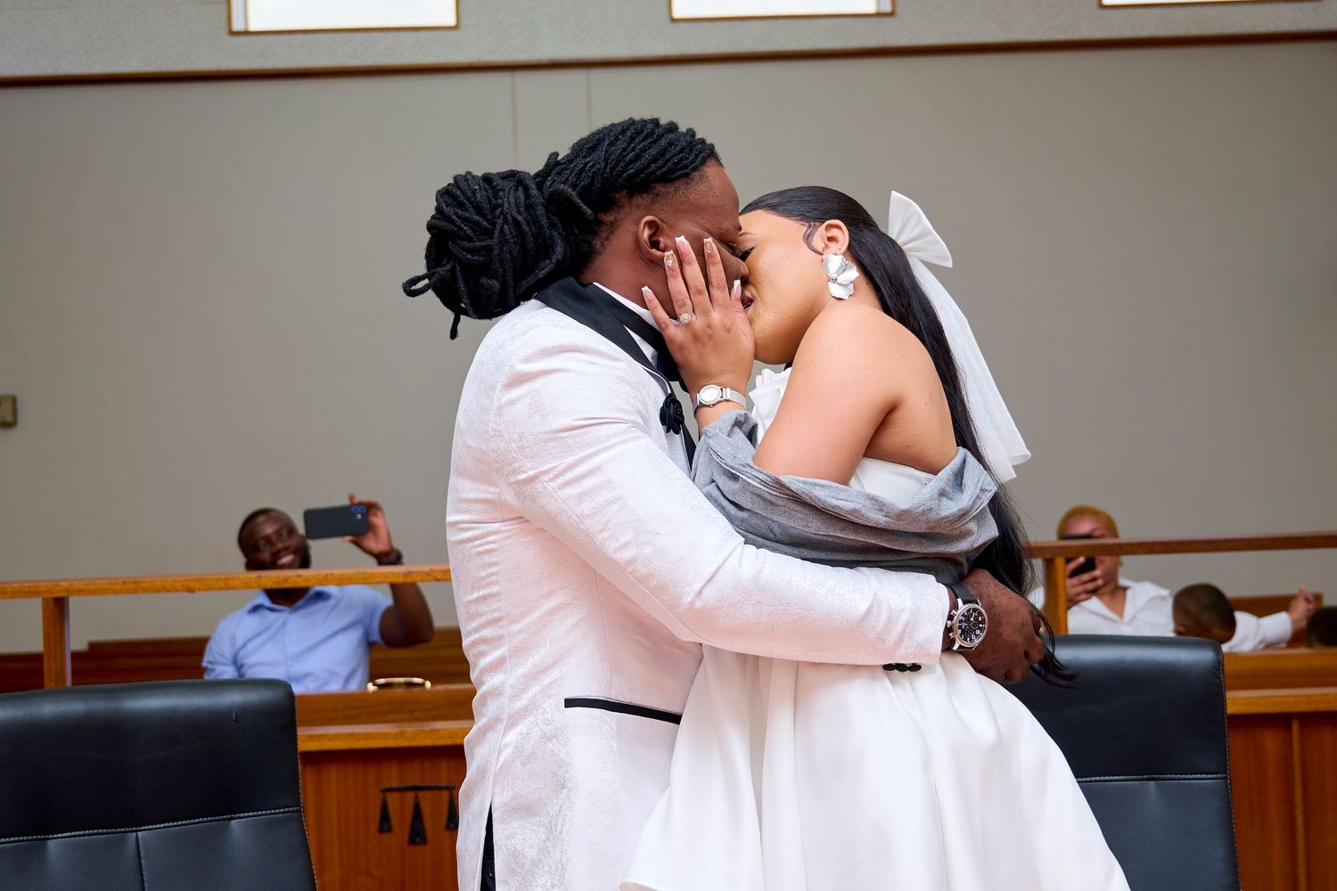 Newlywed couple sharing a first kiss in a courthouse wedding ceremony, bride in white gown, groom in white suit.