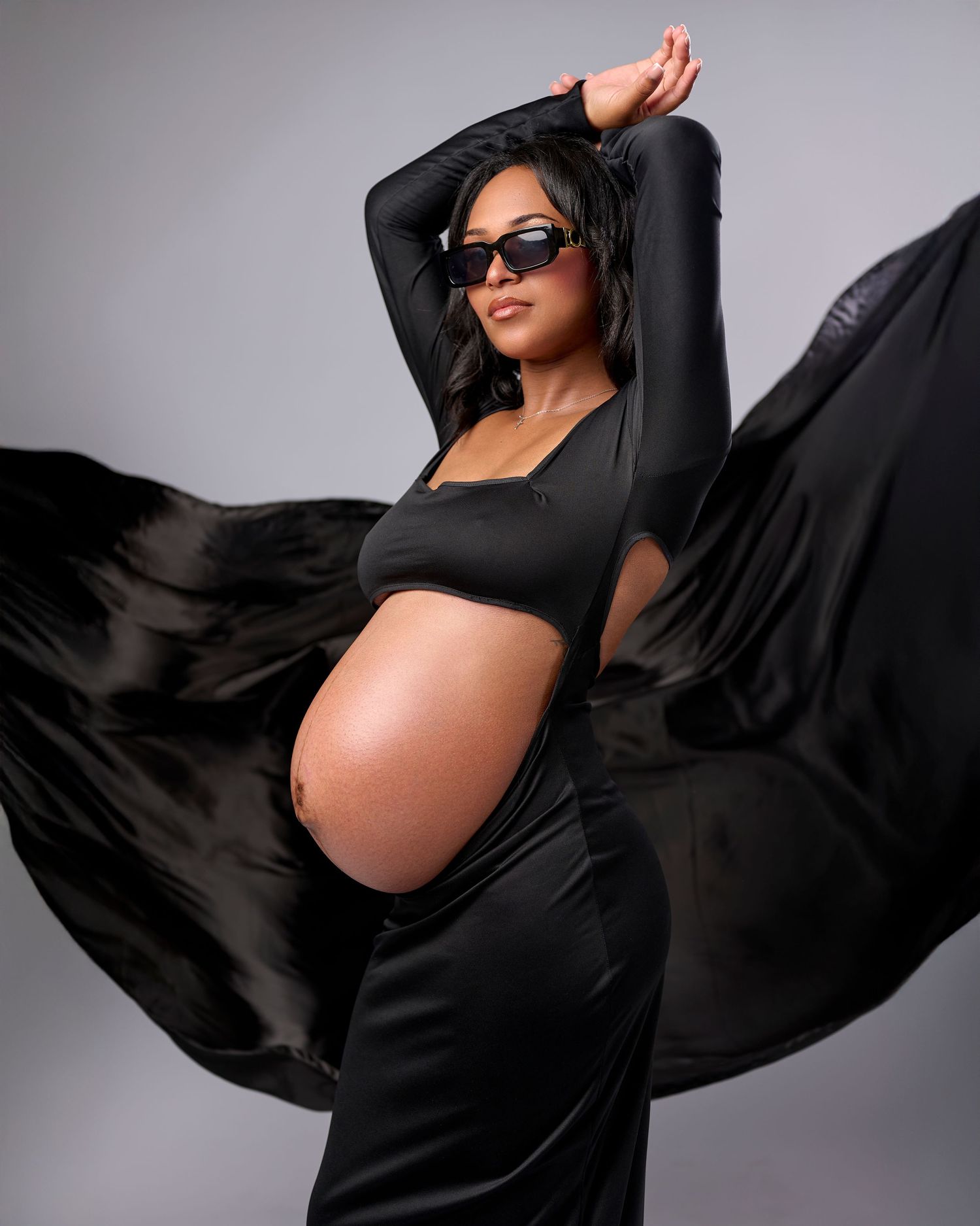 Artistic maternity photoshoot series showing a silhouette in flowing black fabric against a gray studio backdrop.