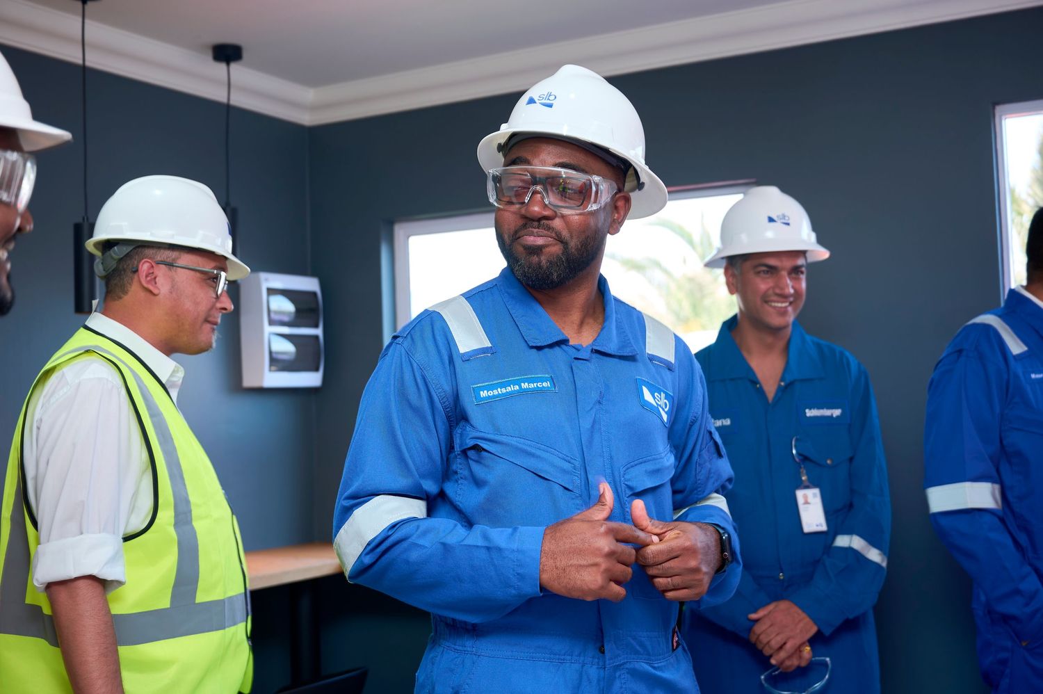 Worker in blue PPE gives thumbs up during industrial site visit.