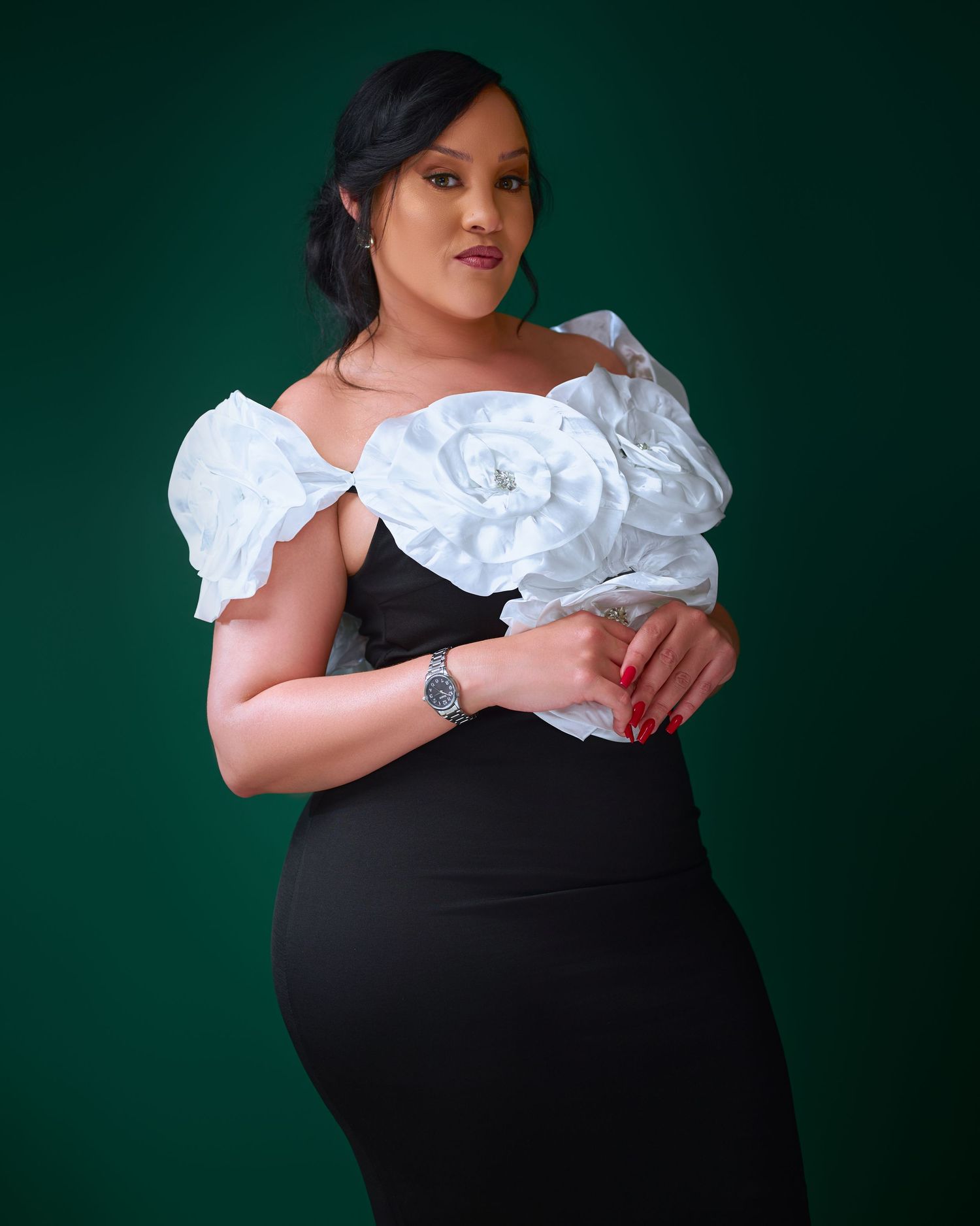 A fashion portrait against a dark green background featuring an elegant black dress with dramatic white ruffled details.