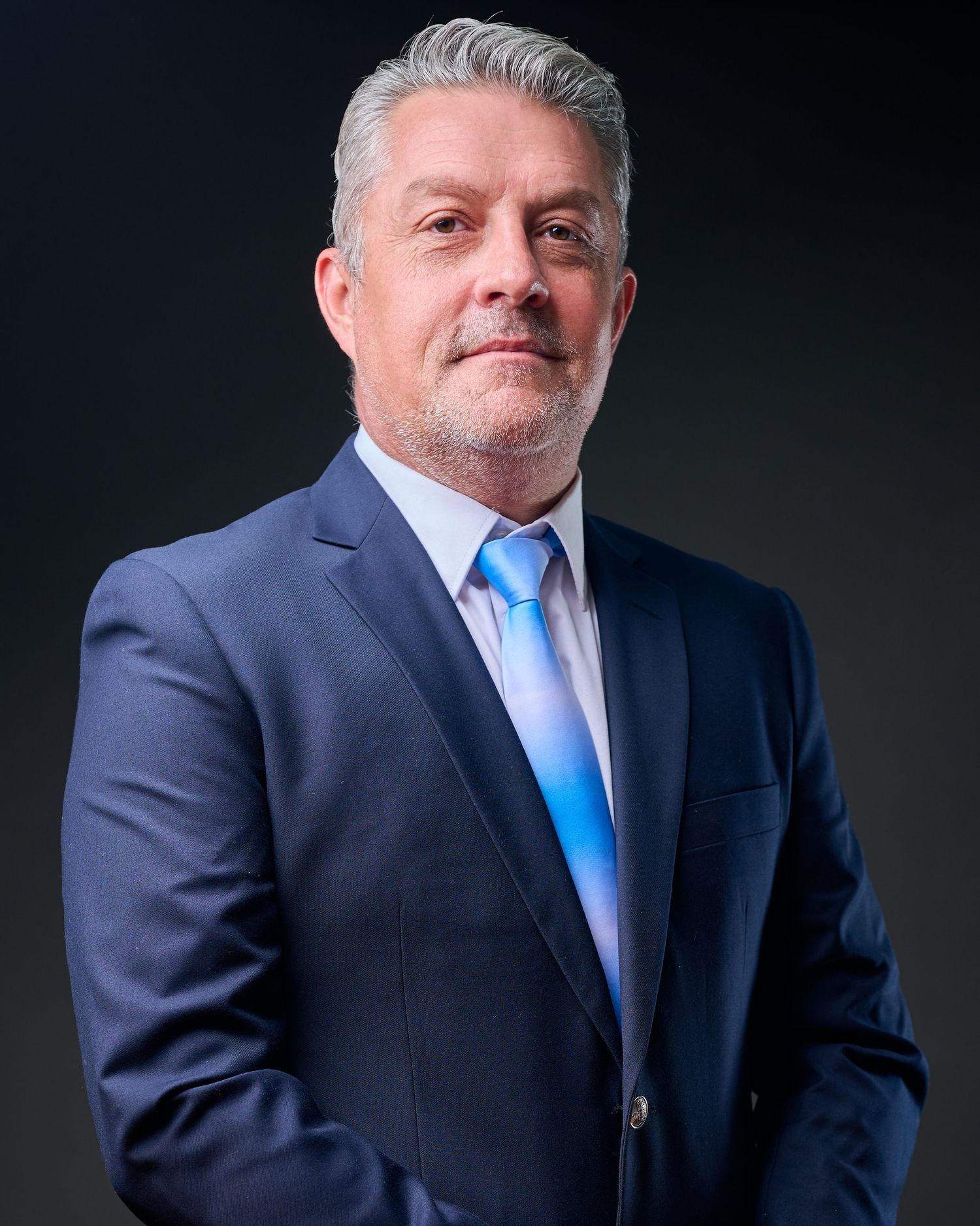 Professional business portrait series showing person in navy suit and blue tie against dark background.