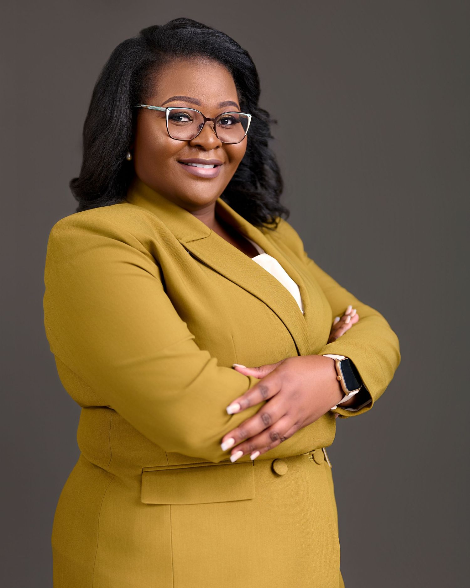 Professional studio portrait in a stylish mustard yellow blazer against a dark grey background.