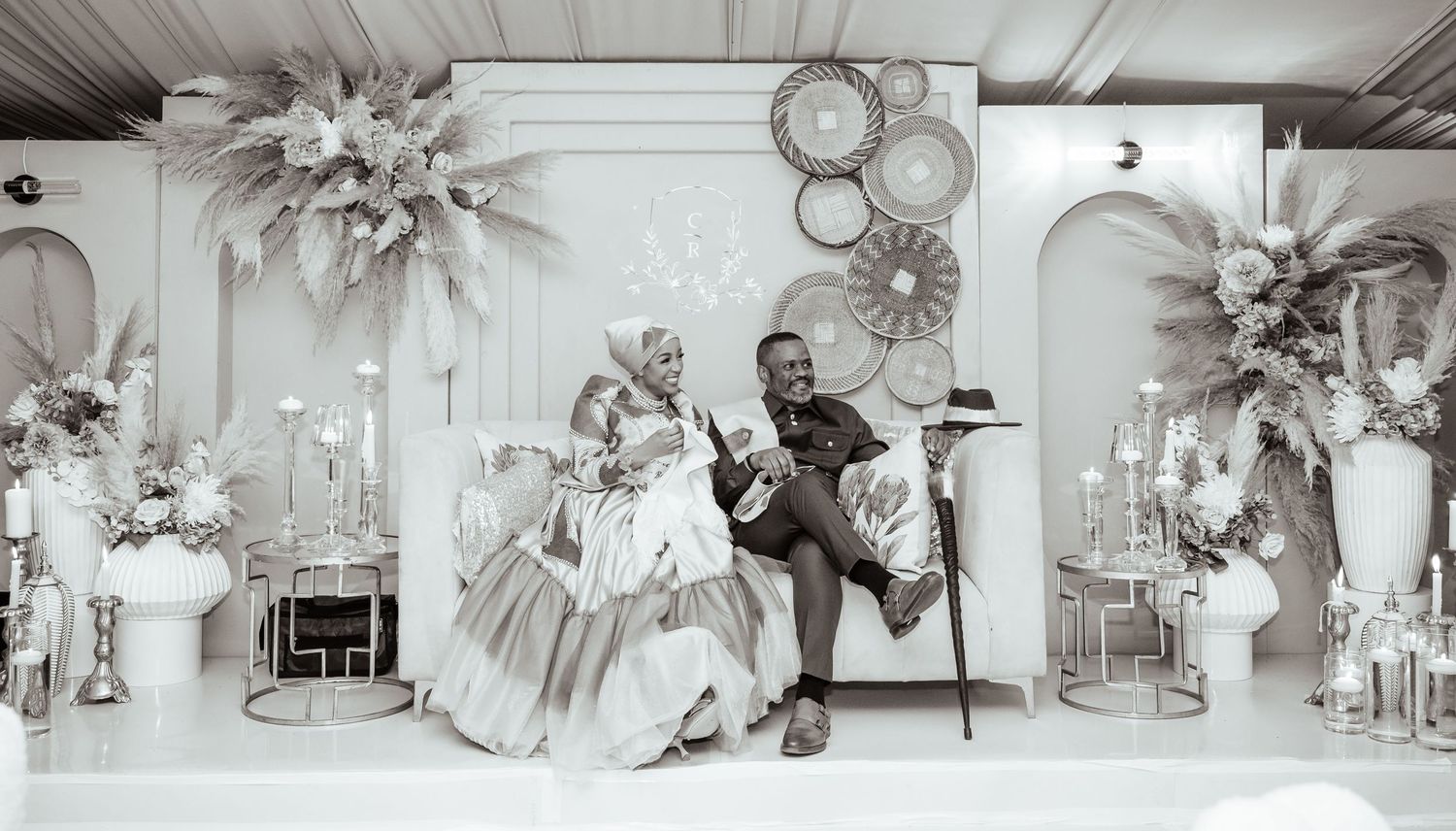 Black and white photo of a couple in elegant attire posing at a beautifully decorated wedding reception venue.