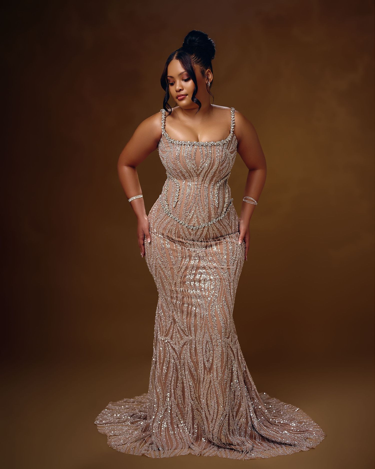 A stunning beaded champagne evening gown with intricate sequin patterns sparkles against a dark brown background.
